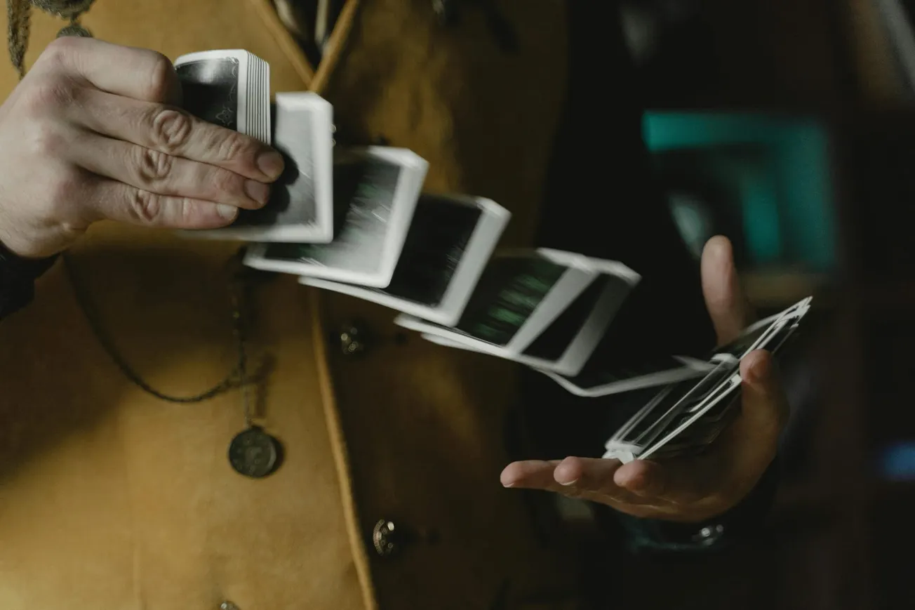 A person wearing a brown vest skillfully fans out playing cards in mid-air, creating a dynamic and mysterious effect, suggesting elegance and dexterity.