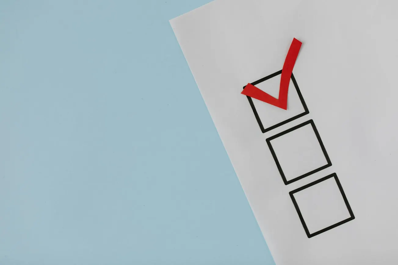 A checklist with three empty boxes on a white paper against a light blue background. The top box has a bold red checkmark, implying completion.