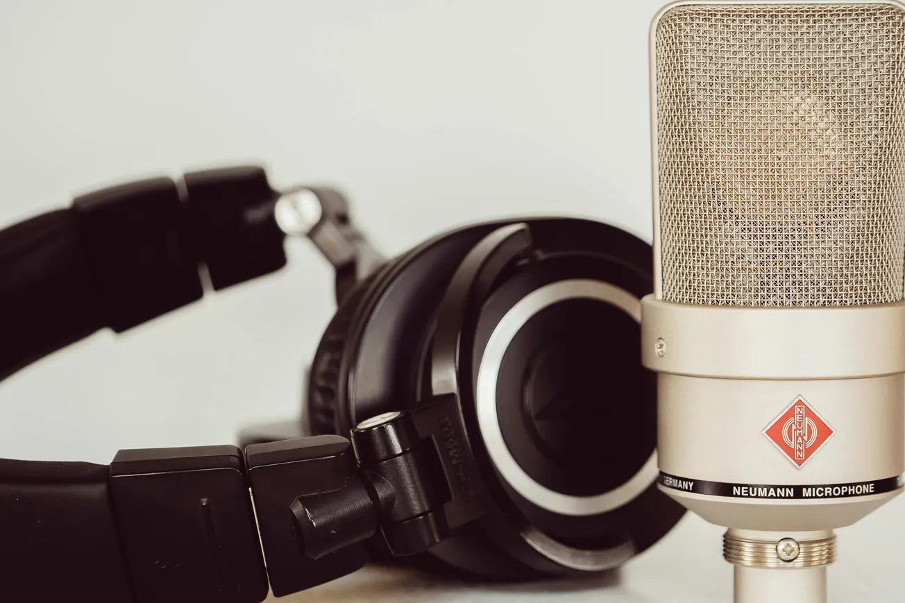 A close-up image of a silver Neumann microphone and black headphones. The setup suggests a professional audio or recording environment.