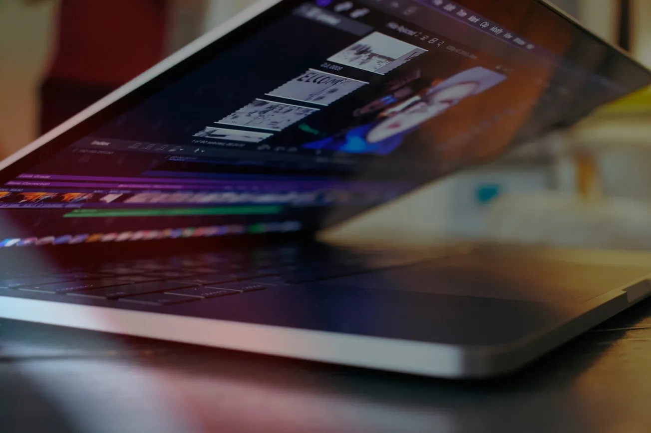 A partially closed laptop displays video editing software on a dimly lit screen, creating a focused and tech-savvy mood. The keyboard and laptop edge are visible.