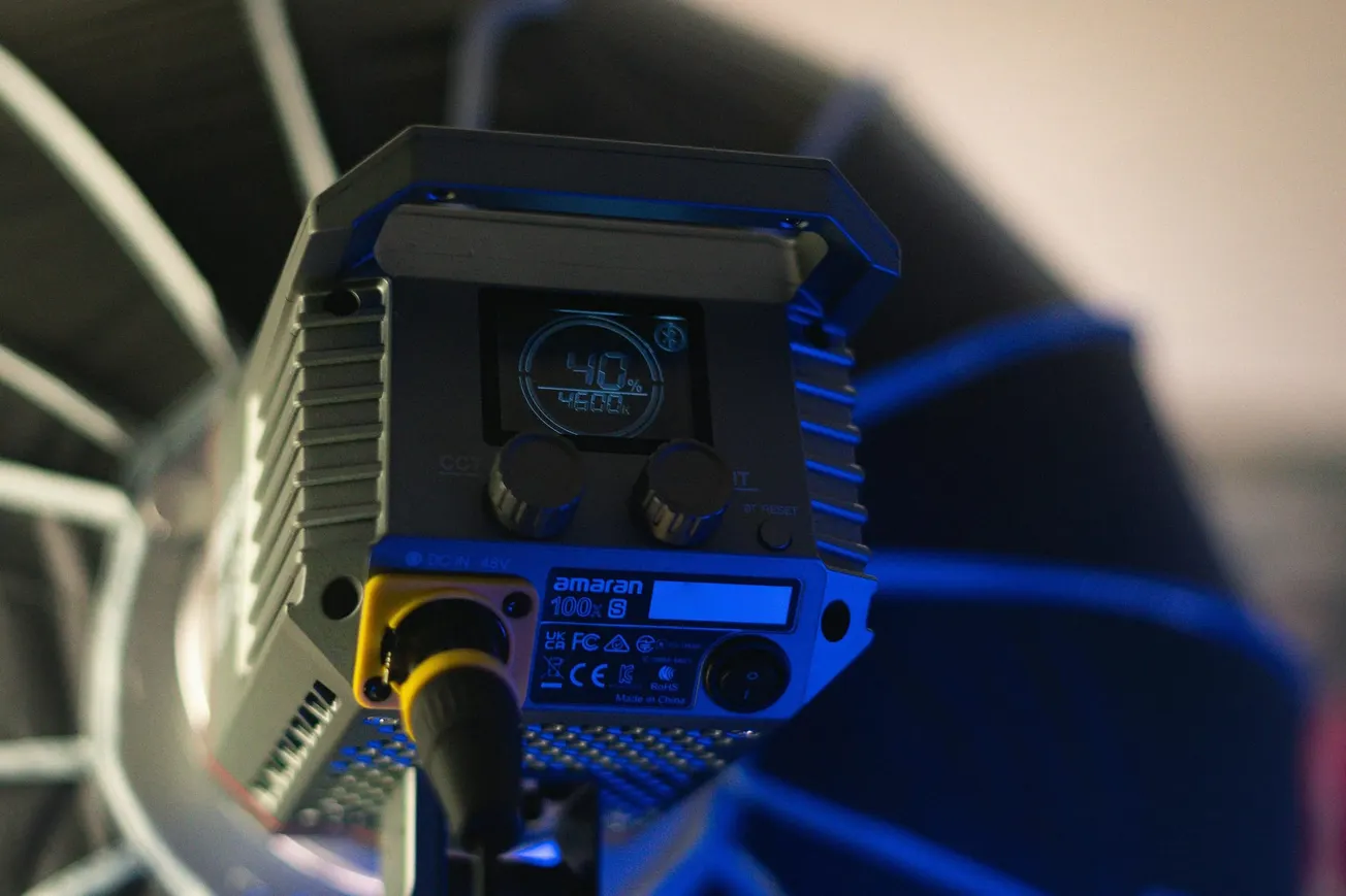 Close-up of a studio light with a digital display showing "40%". The background is softly blurred, with a cool blue tone, conveying a techy ambiance.