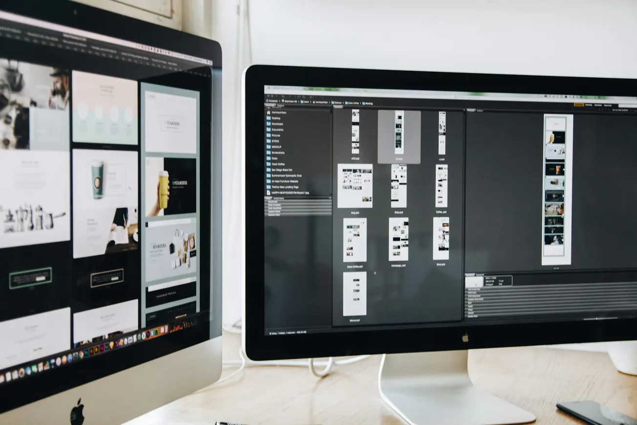 Two computer monitors display website design software. The left screen shows a layout with images and text, while the right screen shows file thumbnails.