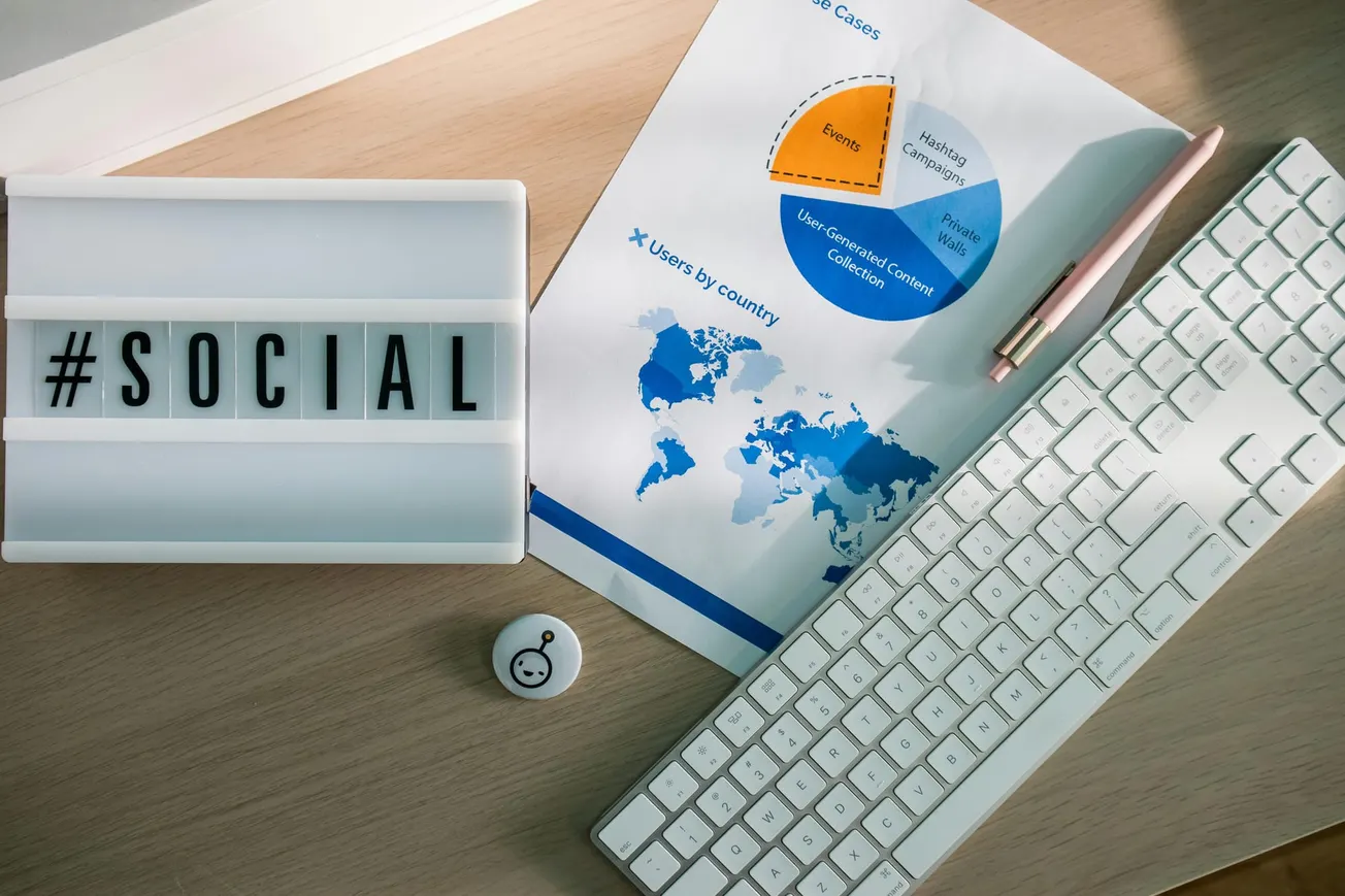 A lightbox with "#SOCIAL" next to a keyboard and paper with a pie chart and world map. A pen and button add a creative, professional vibe.