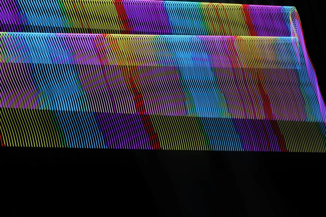 Abstract image of wavy, overlapping neon lines in a spectrum of colors on a black background. The pattern creates a vibrant, dynamic visual effect.