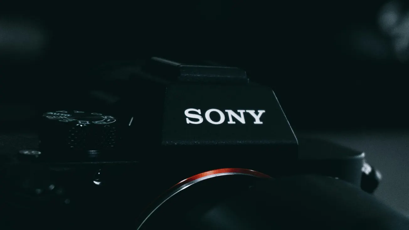 Close-up of a Sony camera in low light, focusing on the logo. The dark tones and slight red accent convey a sleek, professional, and modern feel.