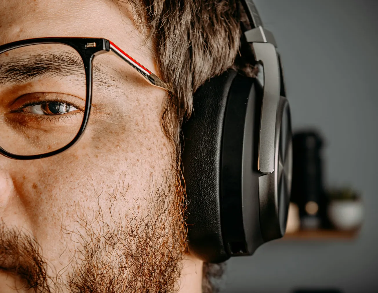 Close-up of a person wearing glasses and large headphones, focusing on their eye and headphones.