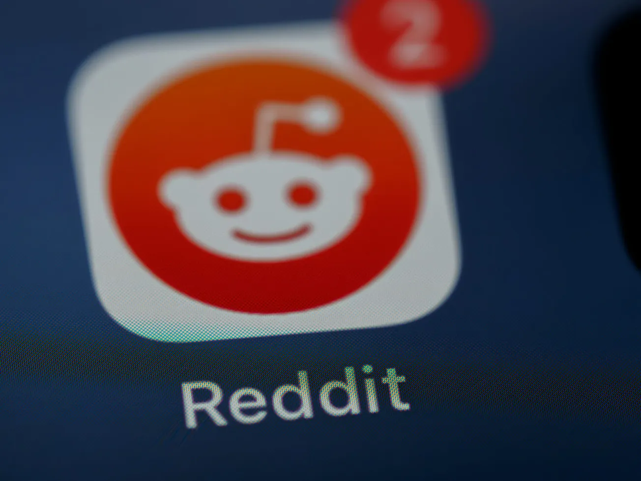 Close-up of the Reddit app icon on a smartphone screen, featuring the smiling Reddit alien mascot. A red notification badge shows the number 2.