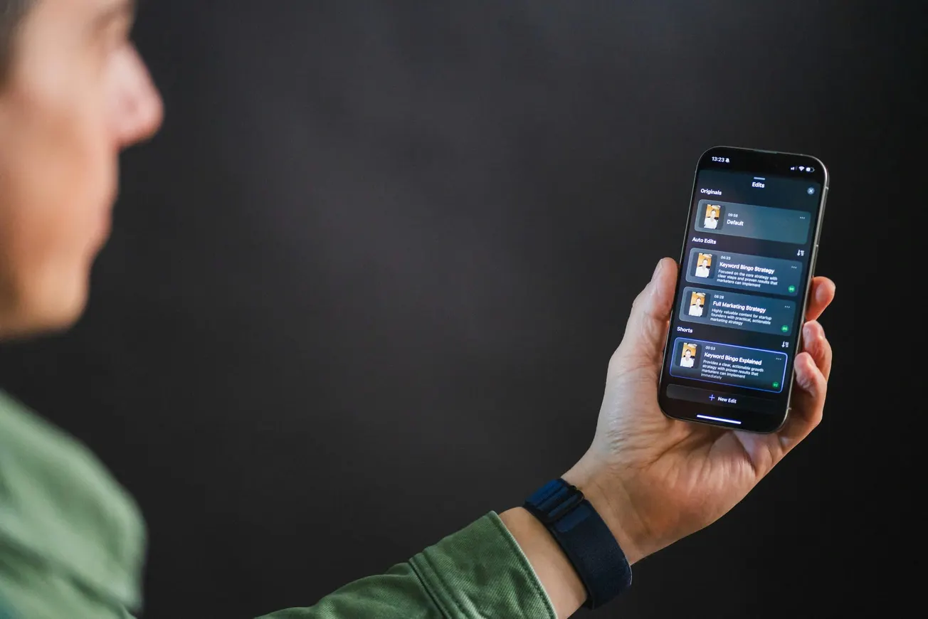 A person in a green jacket holds a smartphone showing a dark-themed app interface with text and icons. The background is softly blurred, creating a focused tone.