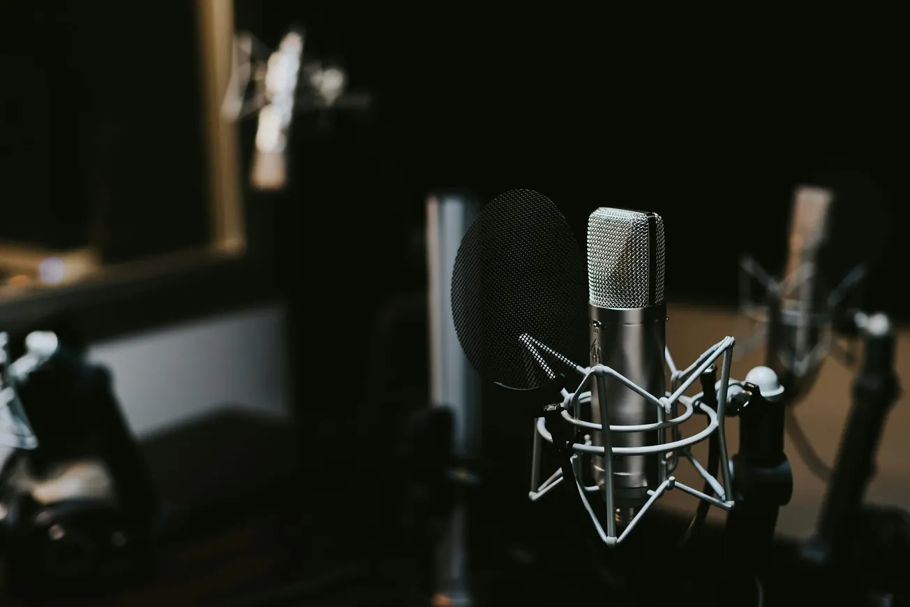 Close-up of a professional microphone with a pop filter in a dimly lit recording studio, creating a focused and intimate atmosphere.
