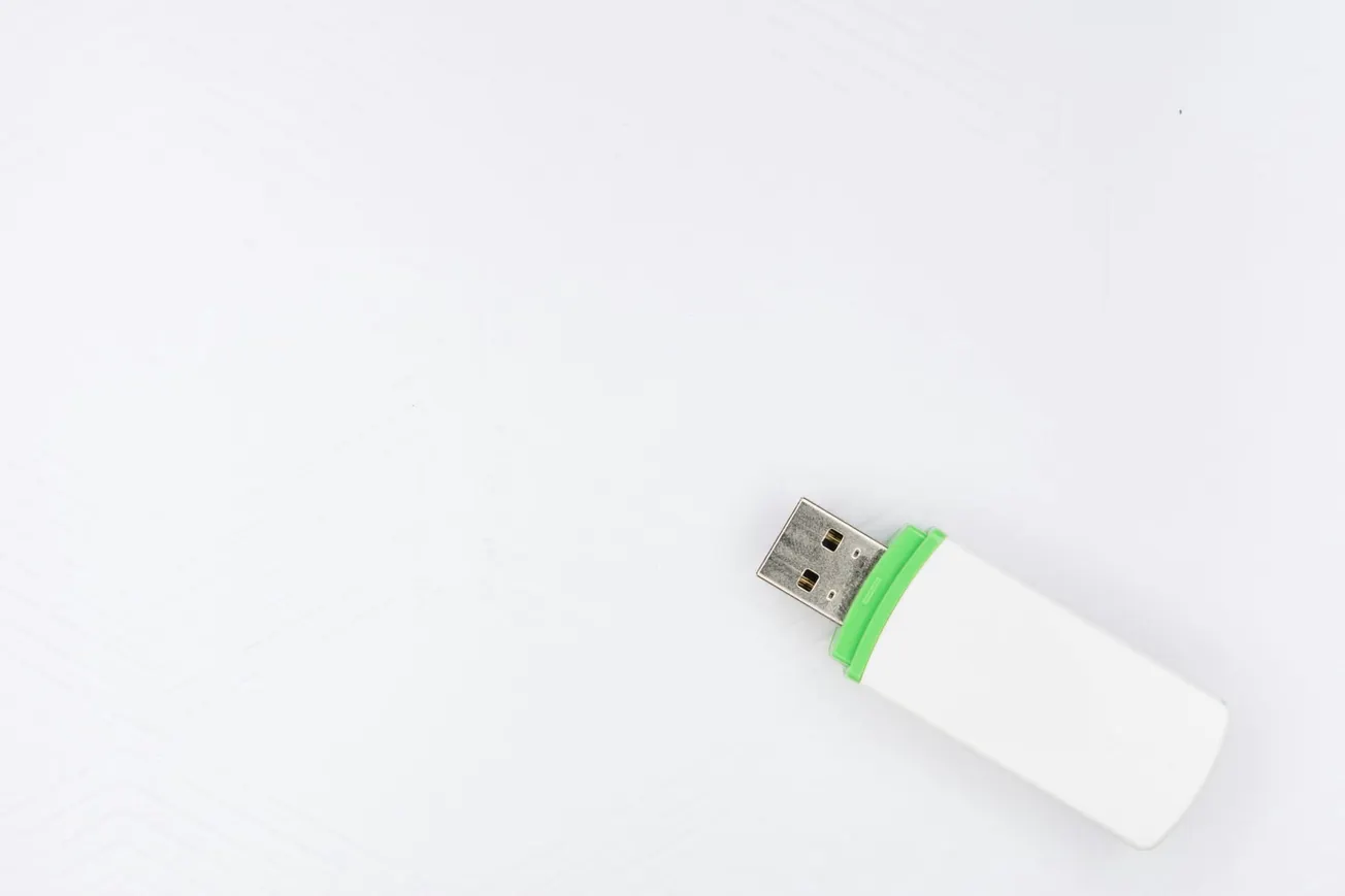 A white USB flash drive with a green accent lies on a white surface, positioned in the bottom right corner, conveying simplicity and minimalism.