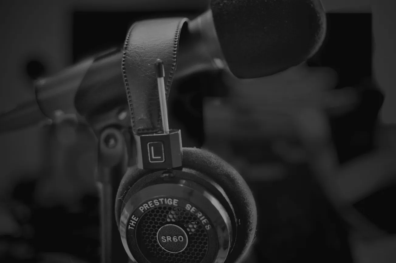 Black and white image of a microphone with a pair of headphones hanging from it. The headphones are labeled "The Prestige Series SR60." Moody and focused.