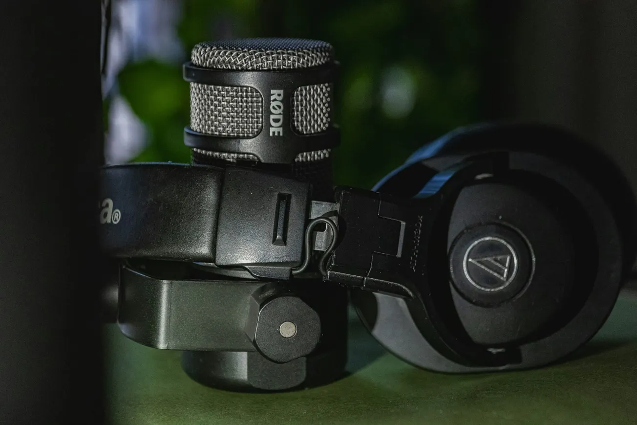 Close-up of a Rode microphone and black headphones lying on a table. The scene is dimly lit, giving a professional and focused ambiance.