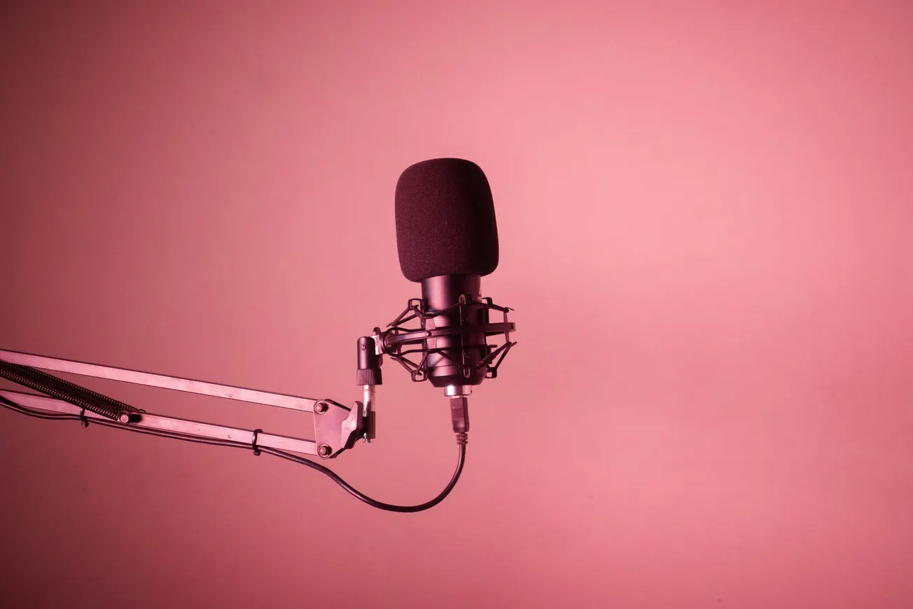 A black microphone on an adjustable stand is set against a pink background. The scene has a professional yet minimalist tone, ideal for podcasts or studios.