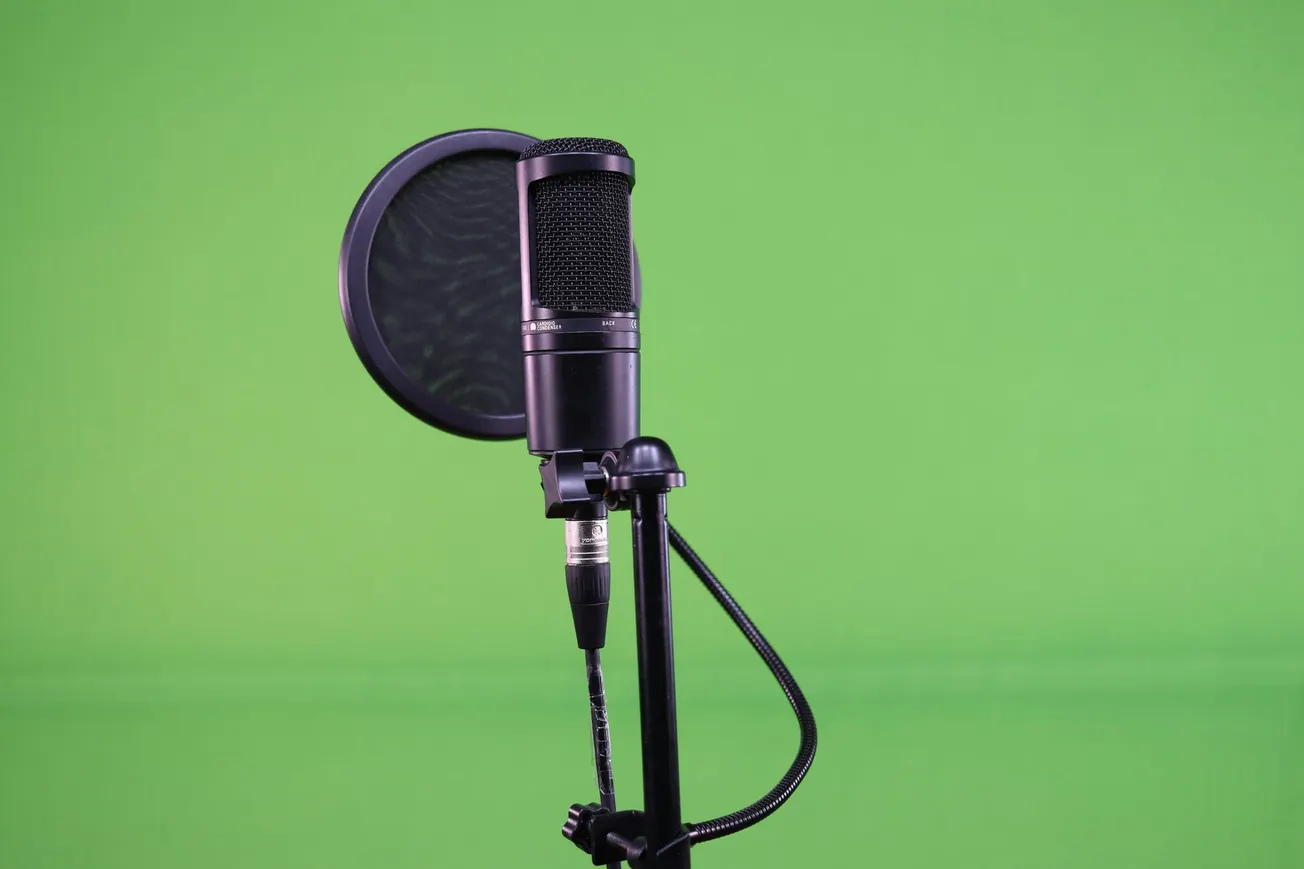 A black studio microphone with a pop filter on a stand is set against a vibrant green background, suggesting a professional recording setting.