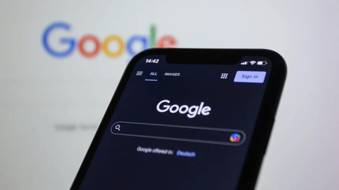 Smartphone displaying Google's search page in dark mode, with the Google logo blurred in the background. The image conveys a tech-focused tone.
