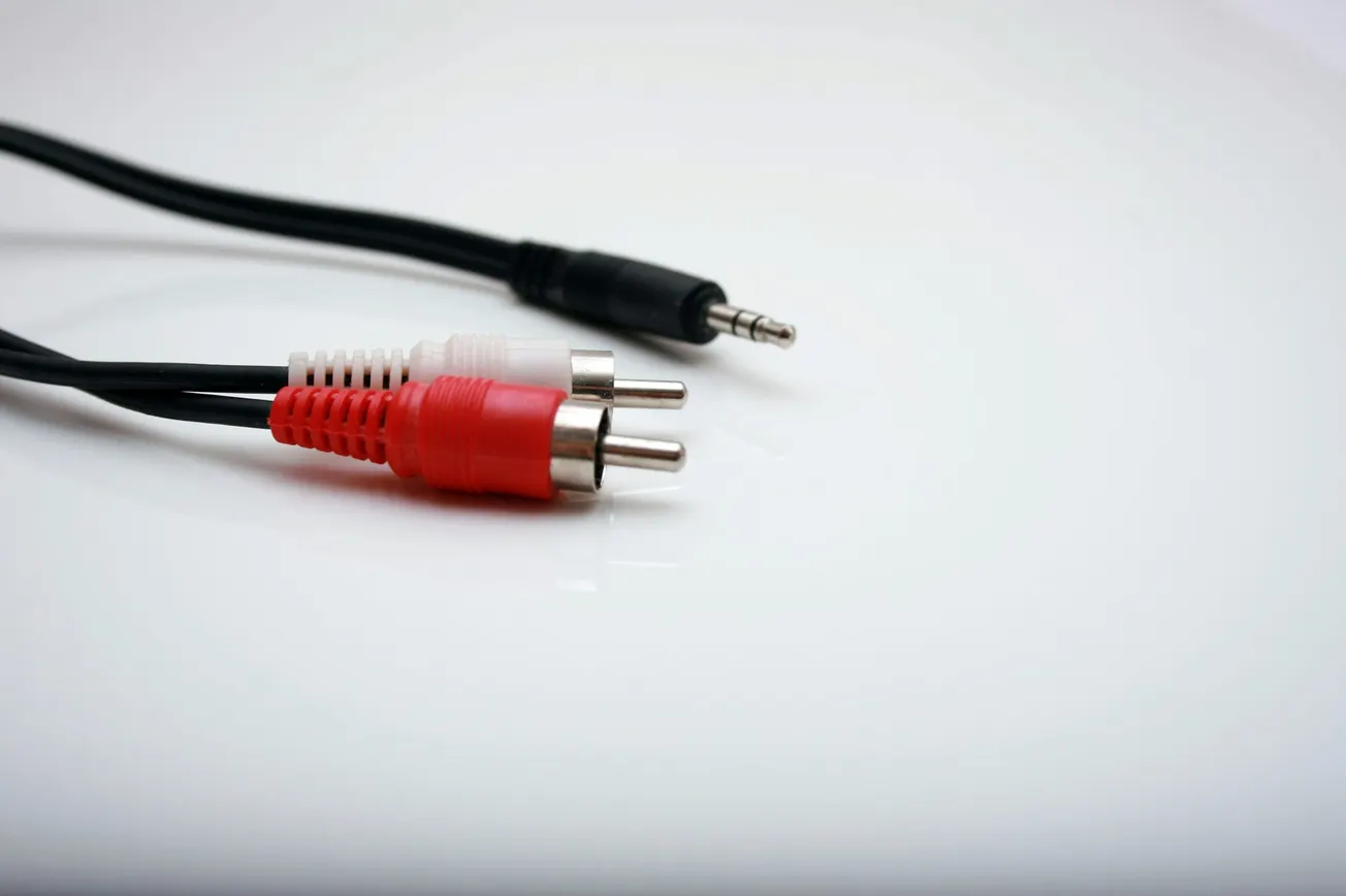 Close-up of a black audio cable with a 3.5mm jack, alongside a red and white RCA connector, on a white glossy surface.