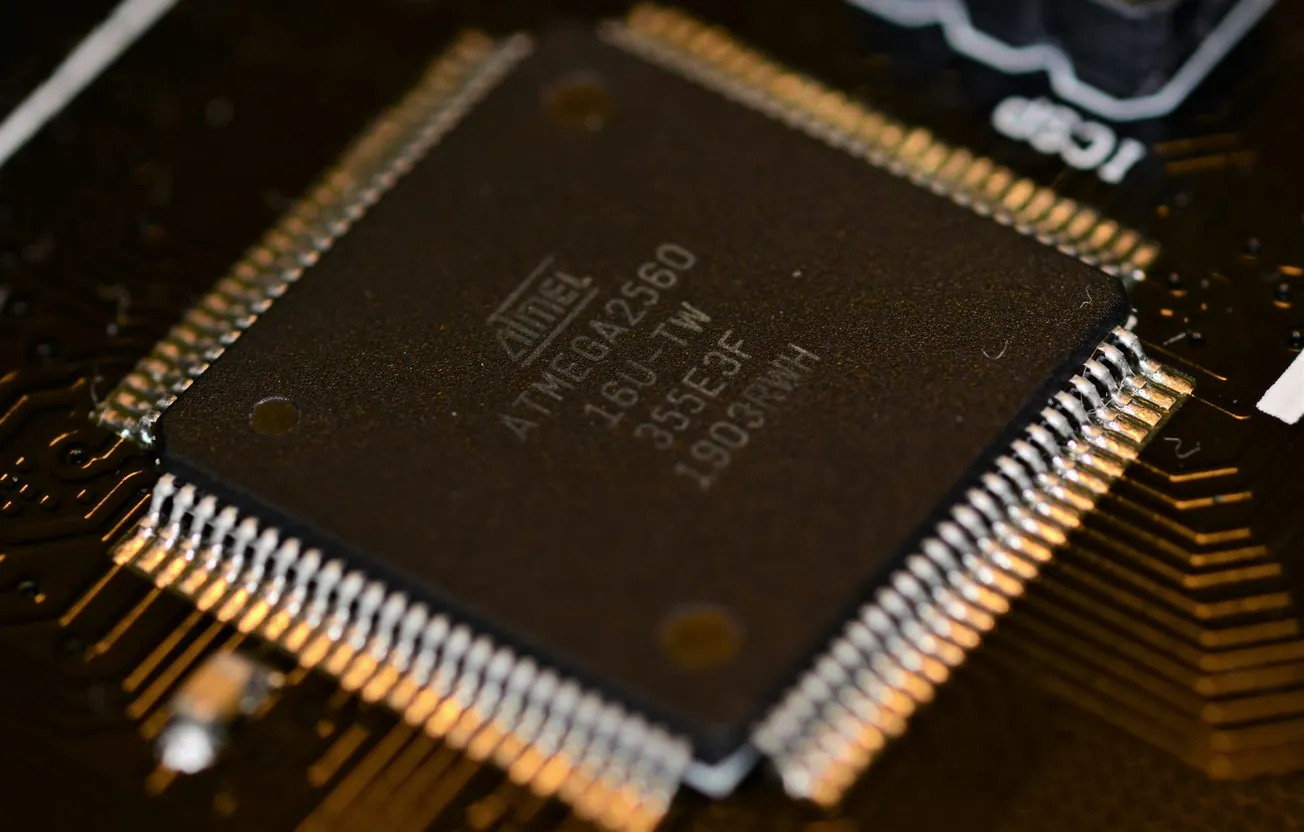 Close-up of a microcontroller with visible pins, marked "ATMEL ATMEGA2560." It rests on a circuit board, highlighting intricate electronic details.