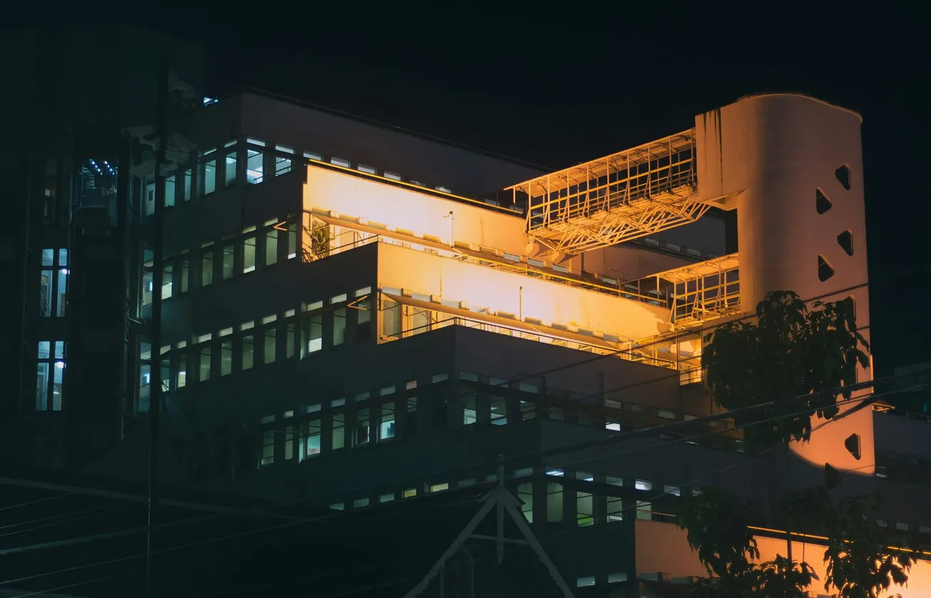 A modern building brightly illuminated at night with warm yellow lights highlighting its geometric structure, conveying a futuristic and vibrant ambiance.