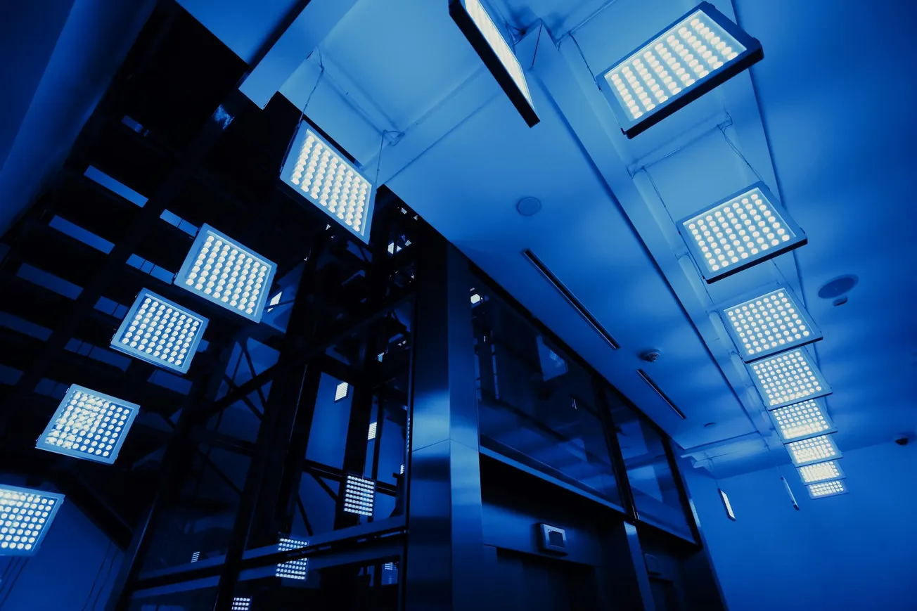 Modern interior with hanging square LED lights, casting a blue hue. Sleek metal structures create a futuristic, minimalist atmosphere.