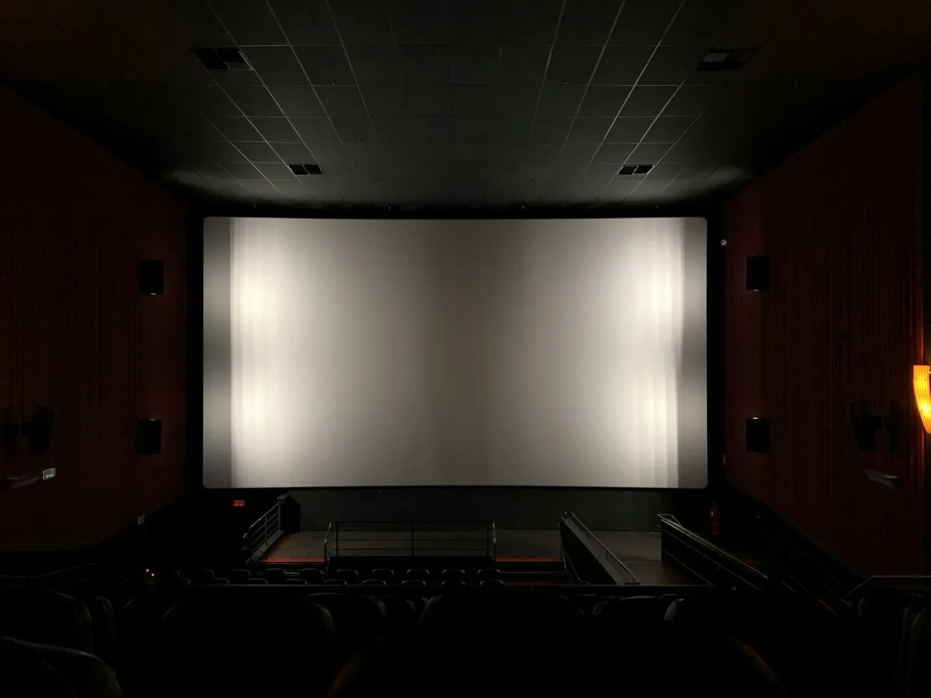 An empty movie theater with a large blank screen, dim ambient lighting, and rows of unoccupied seats creates a calm and expectant atmosphere.