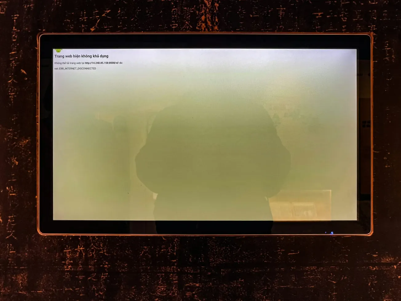 A touch screen displays an error message in Vietnamese on a black, textured background. The reflection of a person is faintly visible on the screen.