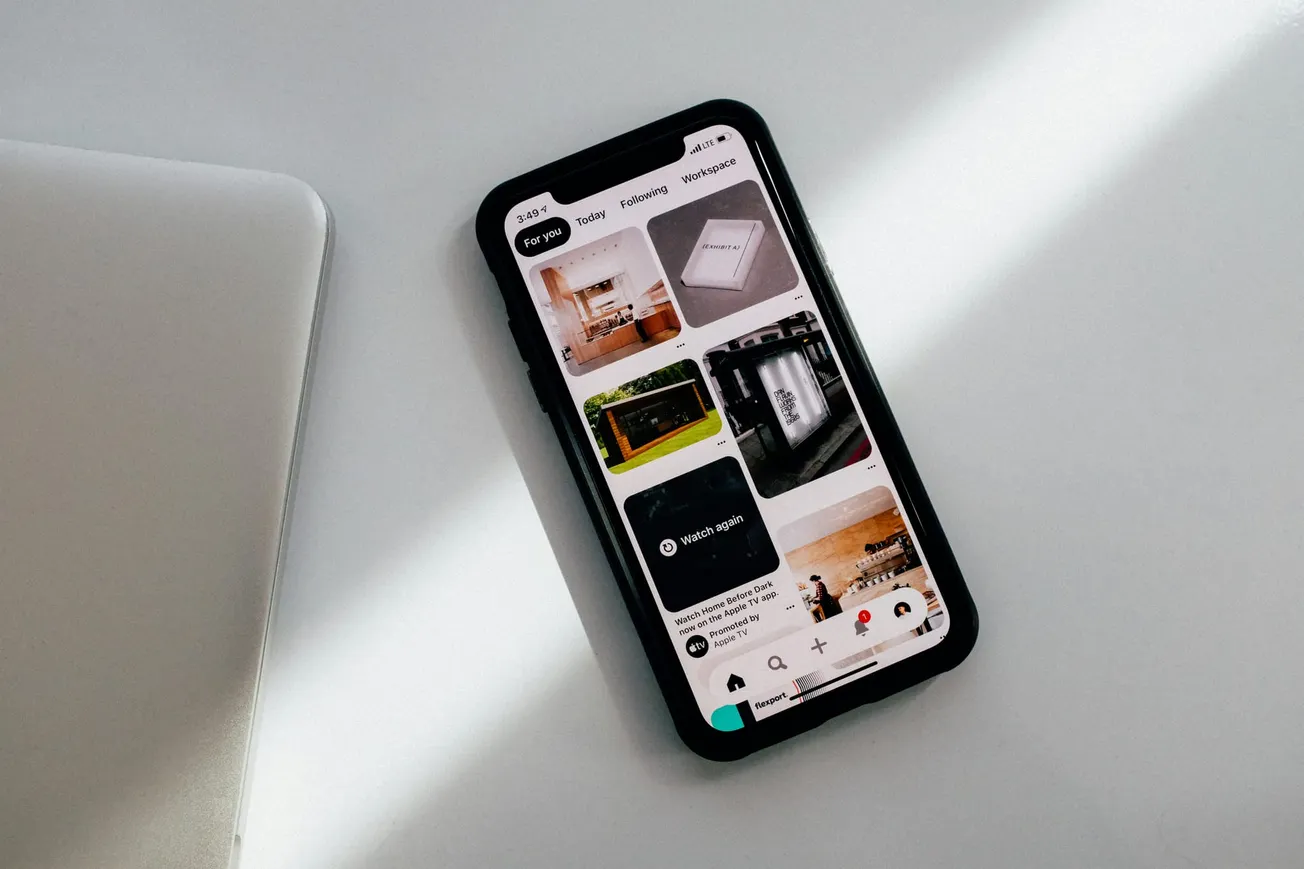 Smartphone displaying Pinterest app with images of interior design and travel inspiration, placed on a white surface, lit by soft daylight.