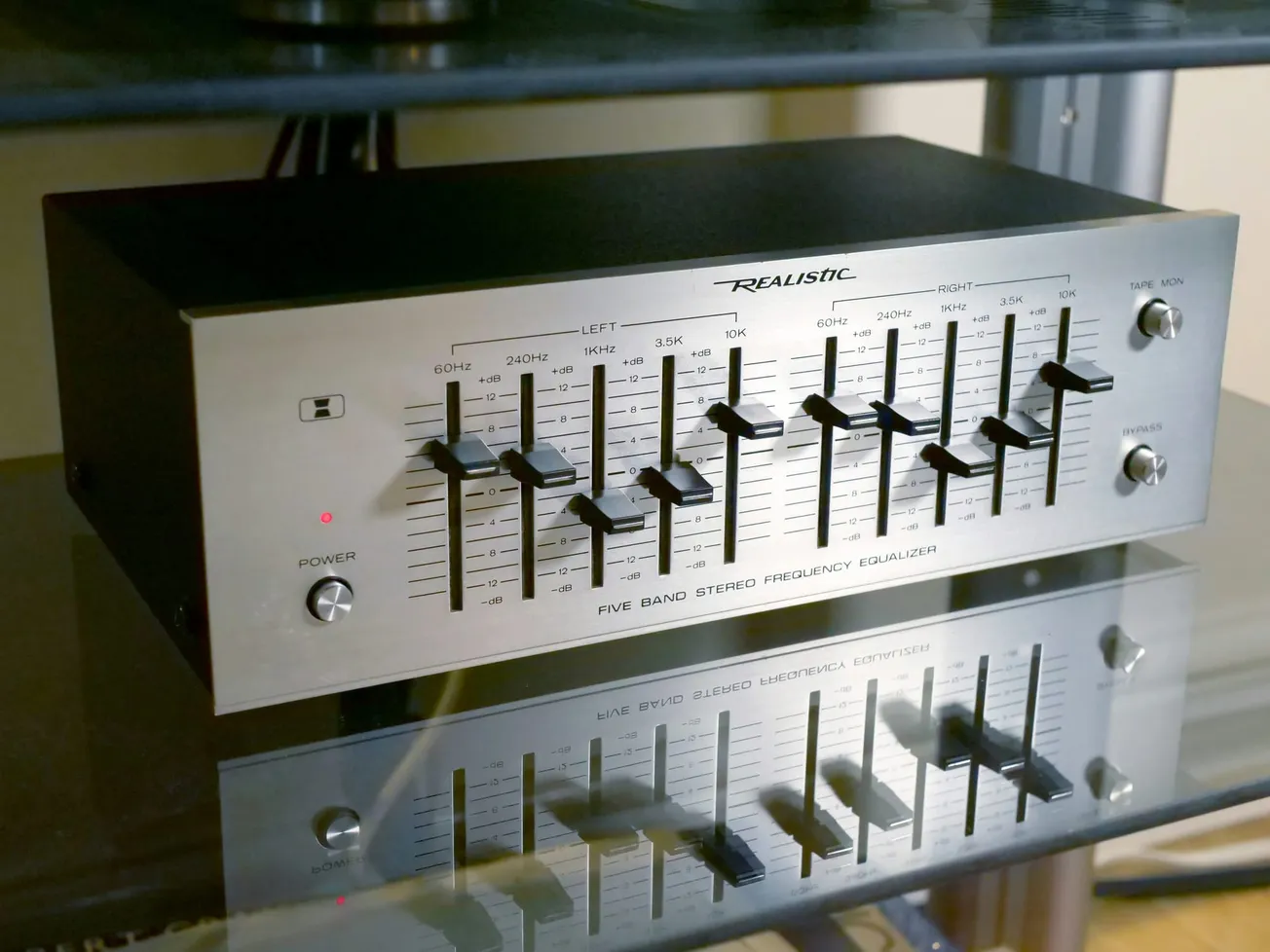 Vintage stereo equalizer with a metal front panel, featuring ten sliders for frequency adjustment, control knobs, and a warm, reflective surface.