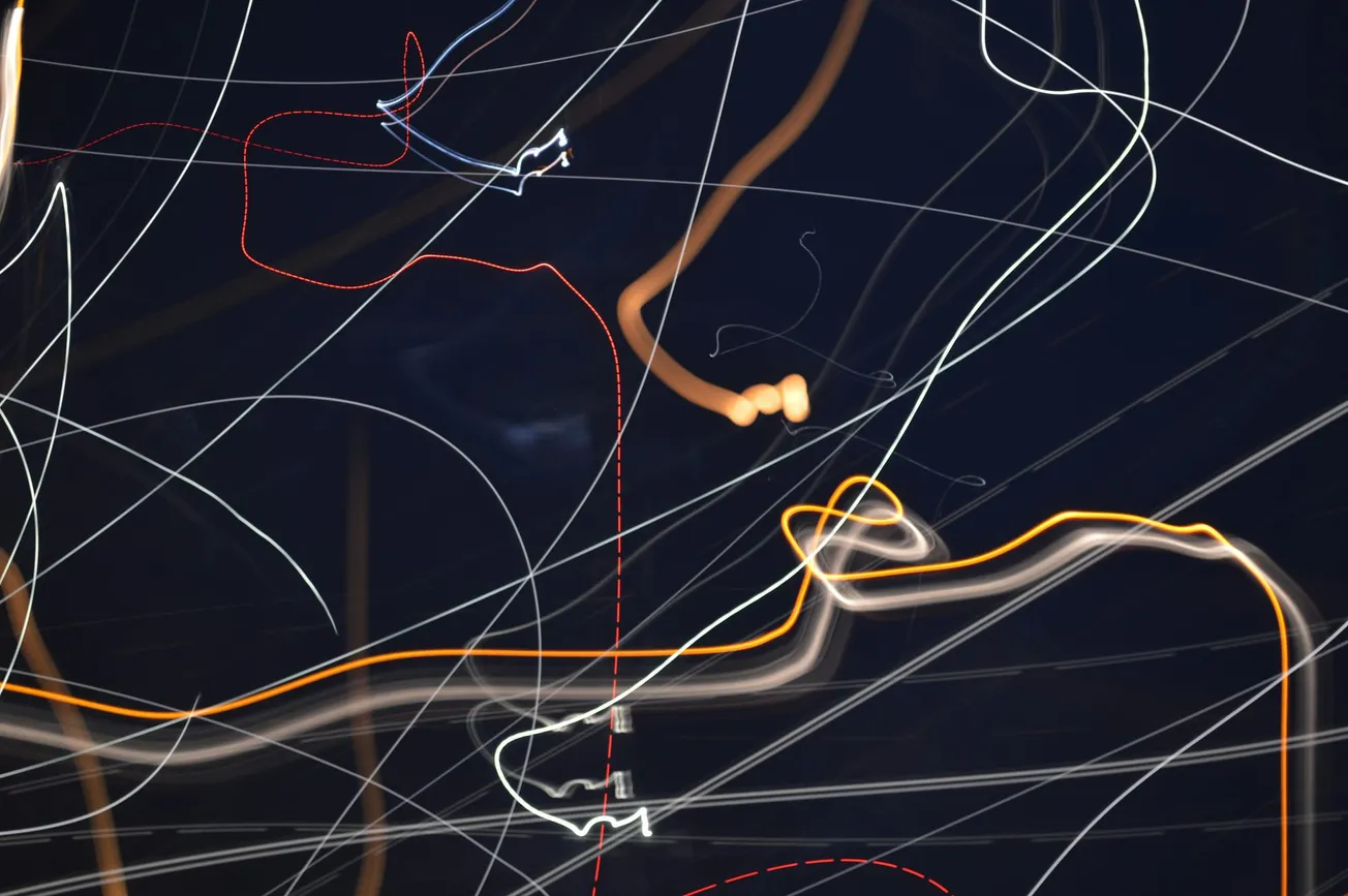 Abstract light painting with streaks of white, orange, and red lines against a dark background, creating a dynamic and chaotic visual effect.