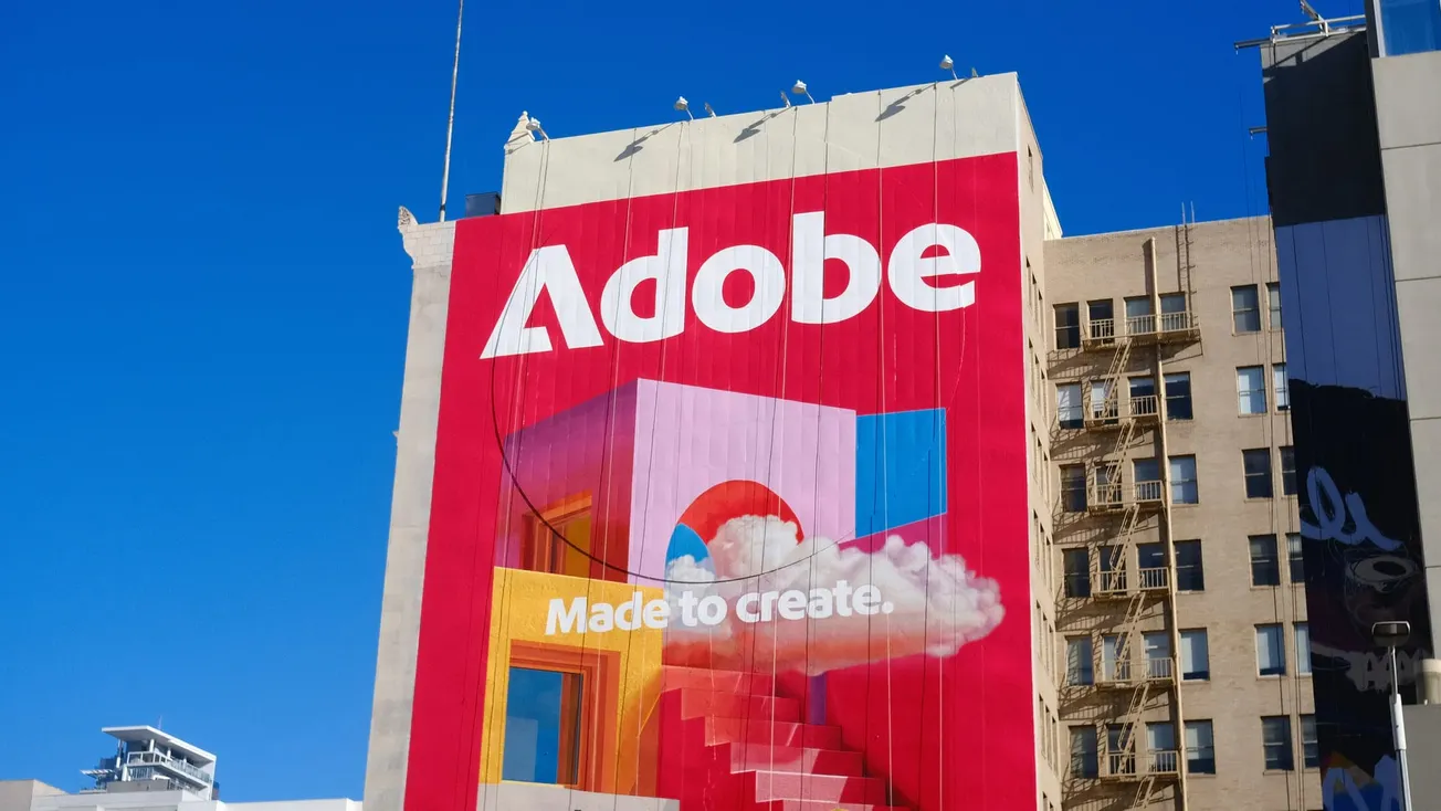A vibrant mural on a tall building displays the word "Adobe" and the phrase "Made to create." Vivid colors and a cloud design evoke creativity.