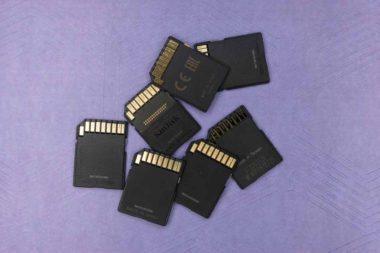 A scattered pile of black SD cards with golden connectors on a purple surface. The tone is organized yet slightly chaotic, evoking a tech-related theme.