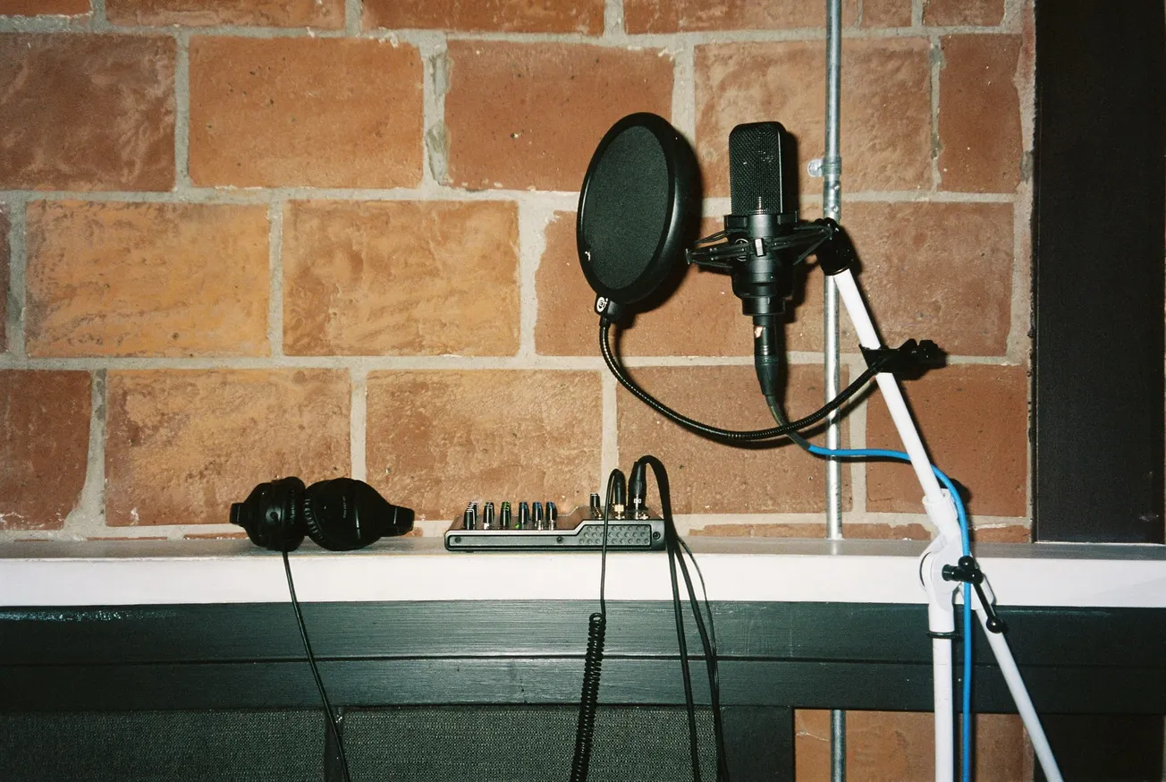 Gemini said Professional podcast recording setup with condenser microphone, pop filter, audio interface, and headphones against a red brick wall.