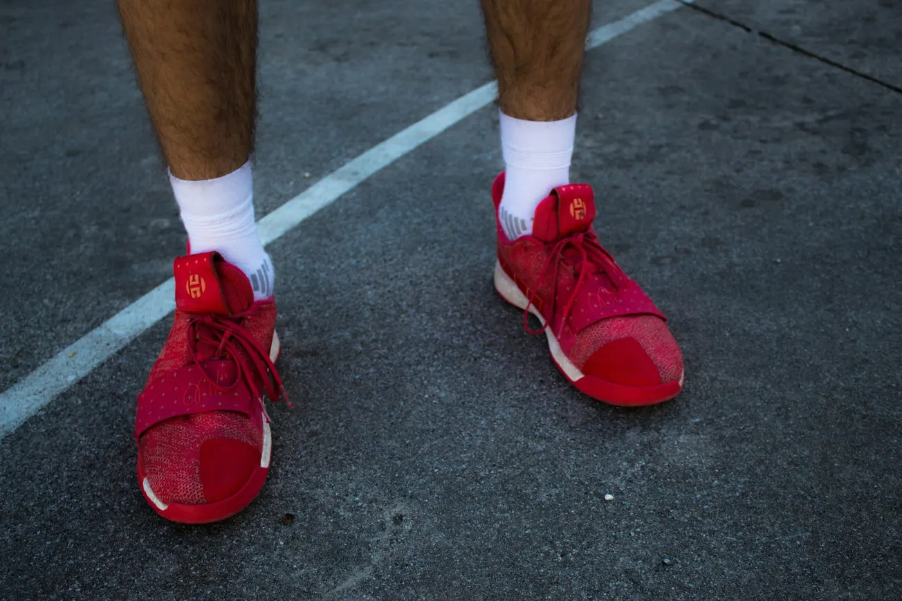 Close-up of a person wearing bright red athletic shoes and white socks standing on a concrete surface, showing part of a basketball court line.