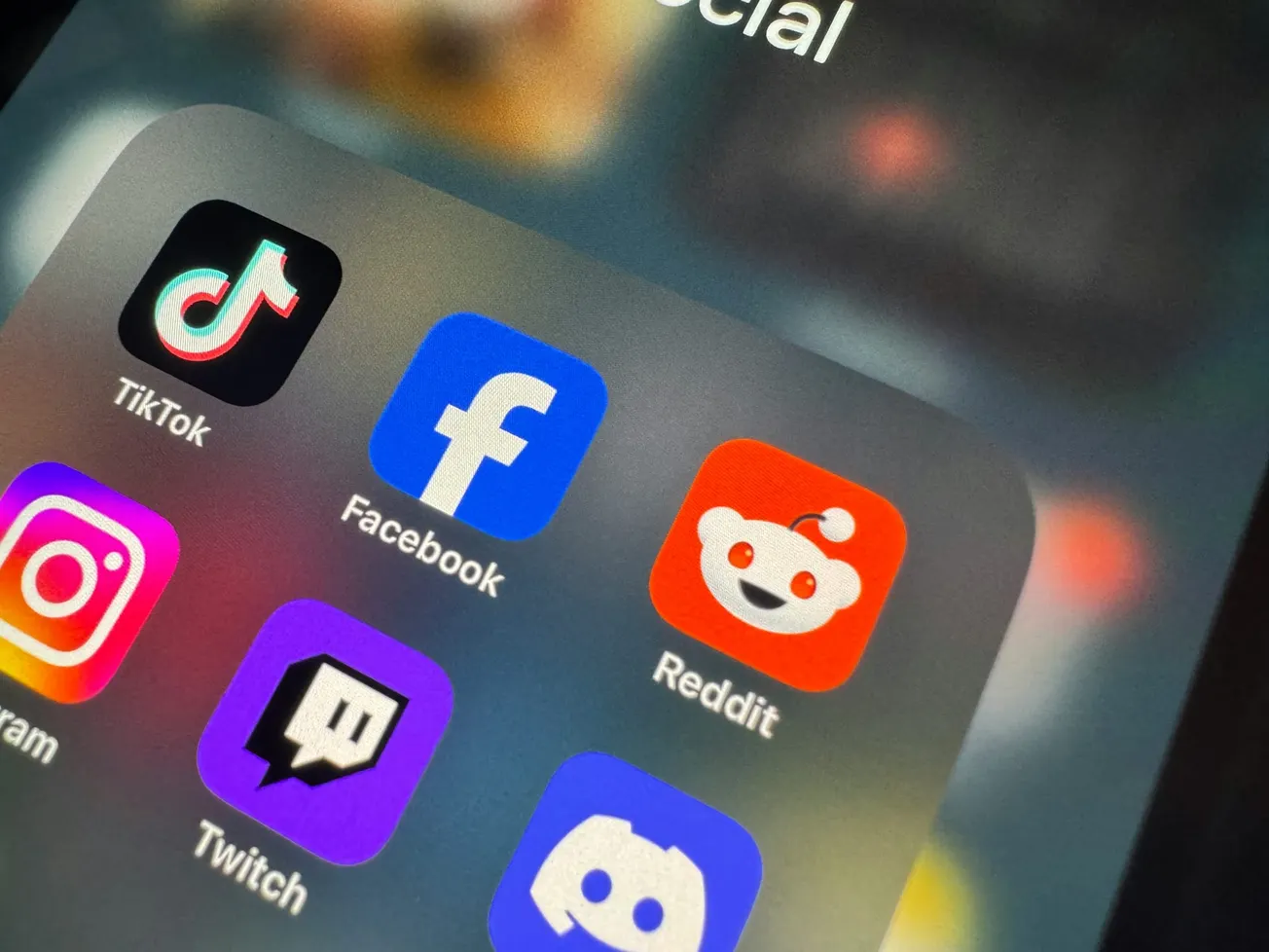Close-up of a smartphone screen showing popular social media app icons including TikTok, Facebook, Instagram, Reddit, Twitch, and Discord.