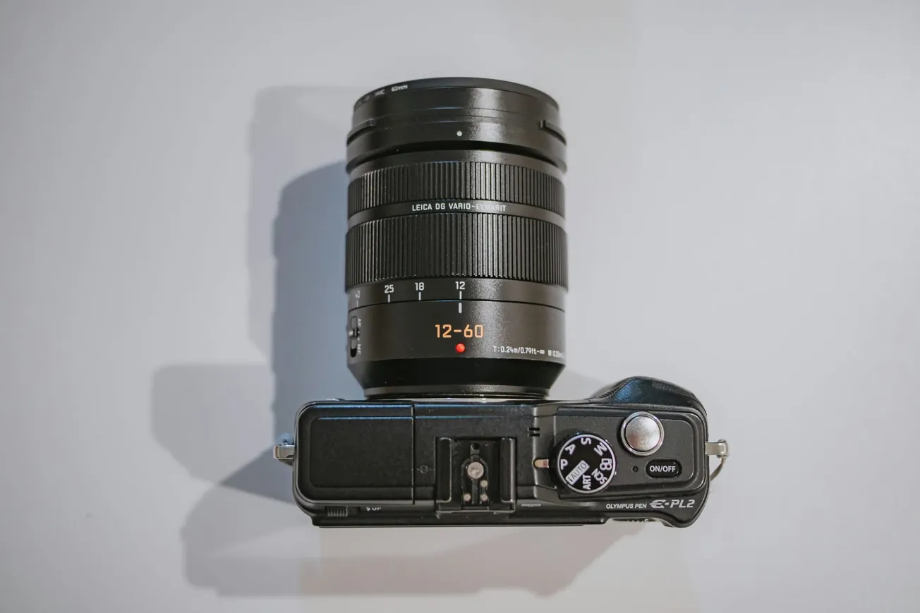 A top view of a camera with a zoom lens. The lens has markings for 12-60mm focal lengths. The camera has a mode dial and on/off switch.