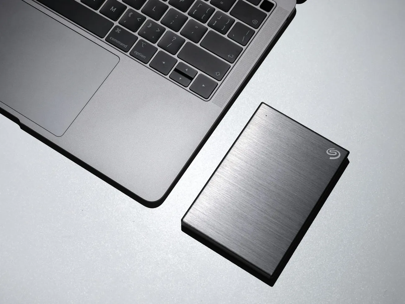 Laptop keyboard and sleek external hard drive placed on a reflective surface. The minimalist design conveys a modern, tech-savvy feel.