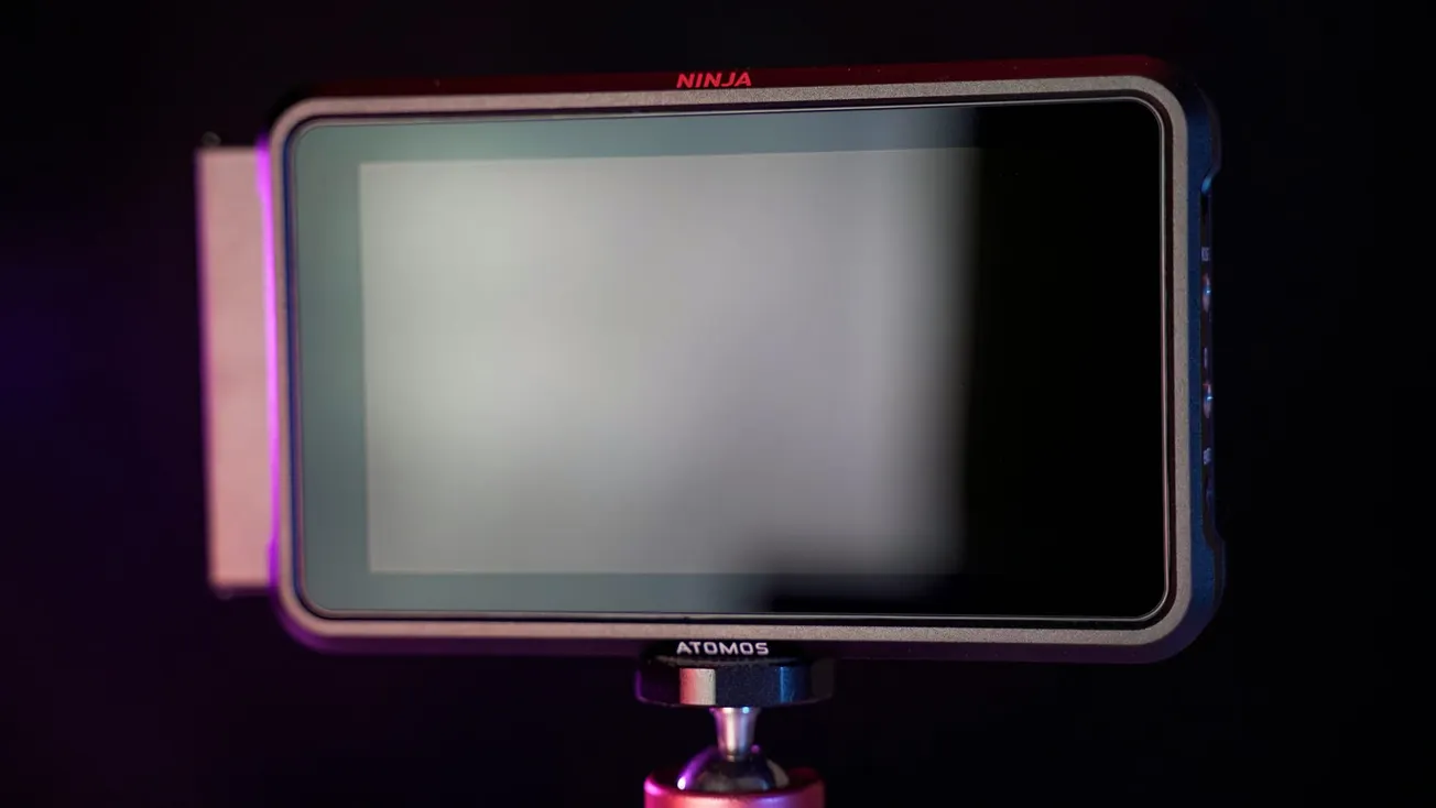 A black video monitor labeled "Ninja" with a reflective screen, mounted on a tripod against a dark background, with subtle purple lighting.