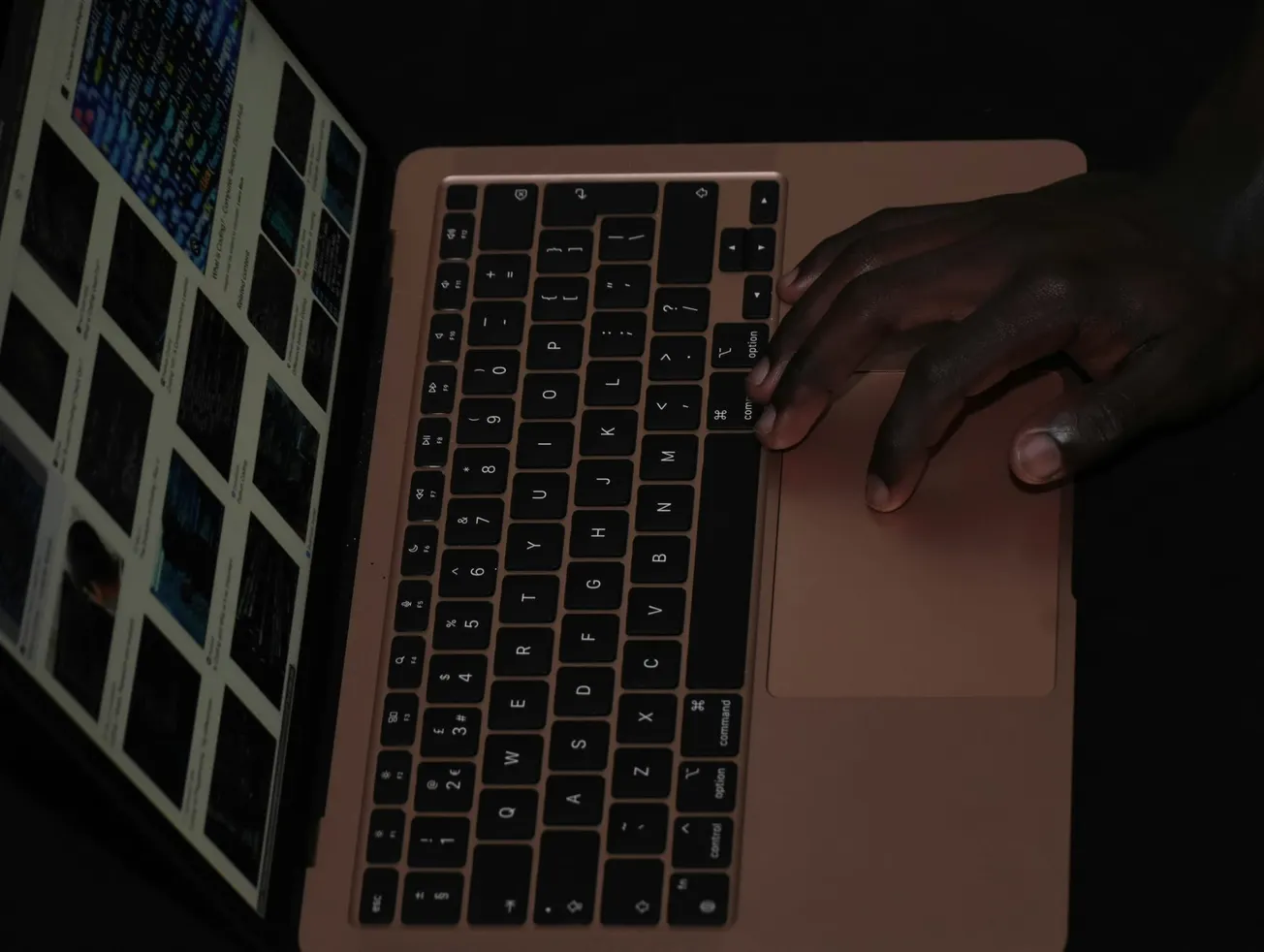 A hand types on a laptop with a bronze keyboard. The screen displays images on a dark background, suggesting focused work or browsing.