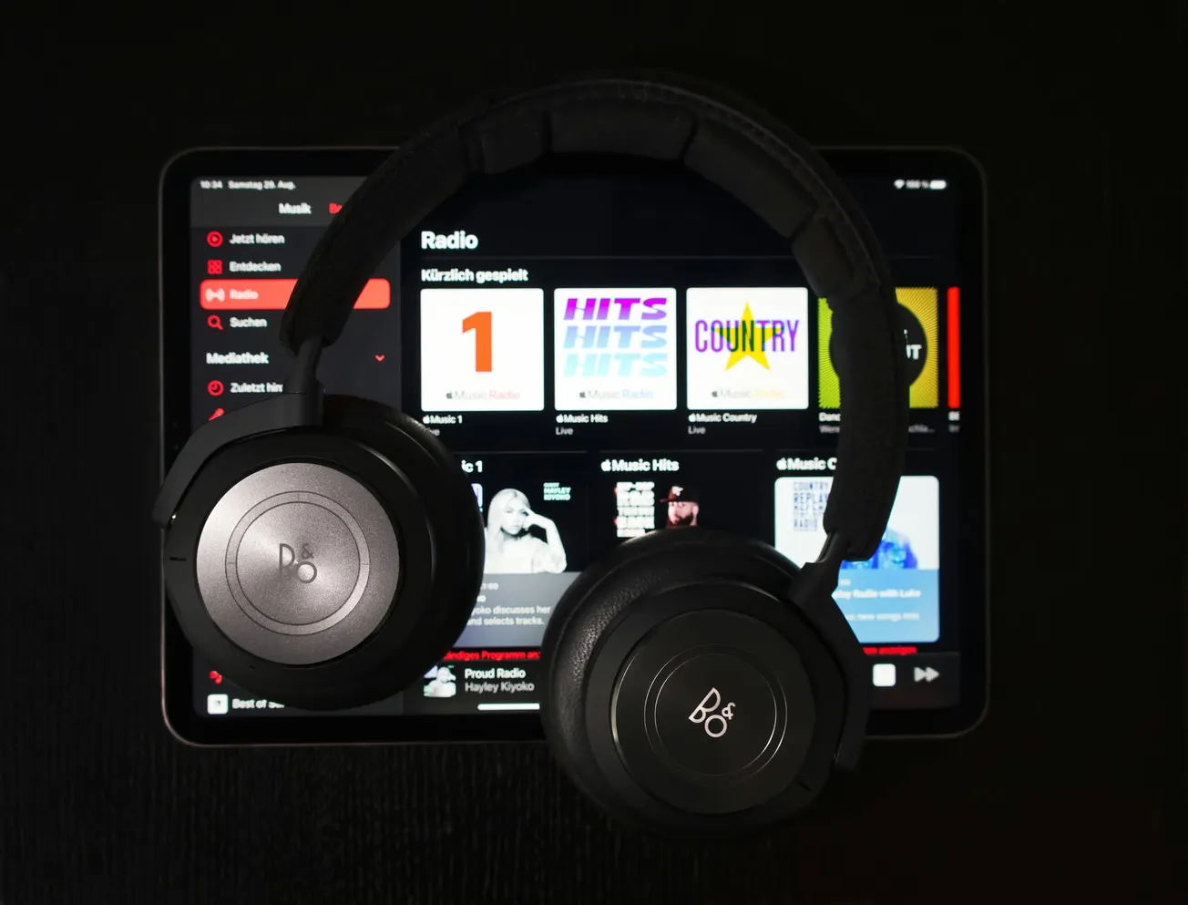 Headphones resting on a tablet displaying a music streaming app. The screen shows various playlists, creating a modern and tech-focused ambience.