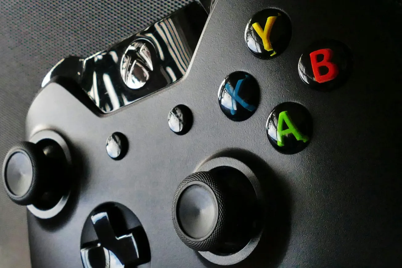 Close-up of a black game controller showing colorful buttons labeled Y, B, X, and A, alongside analog sticks and a textured surface.