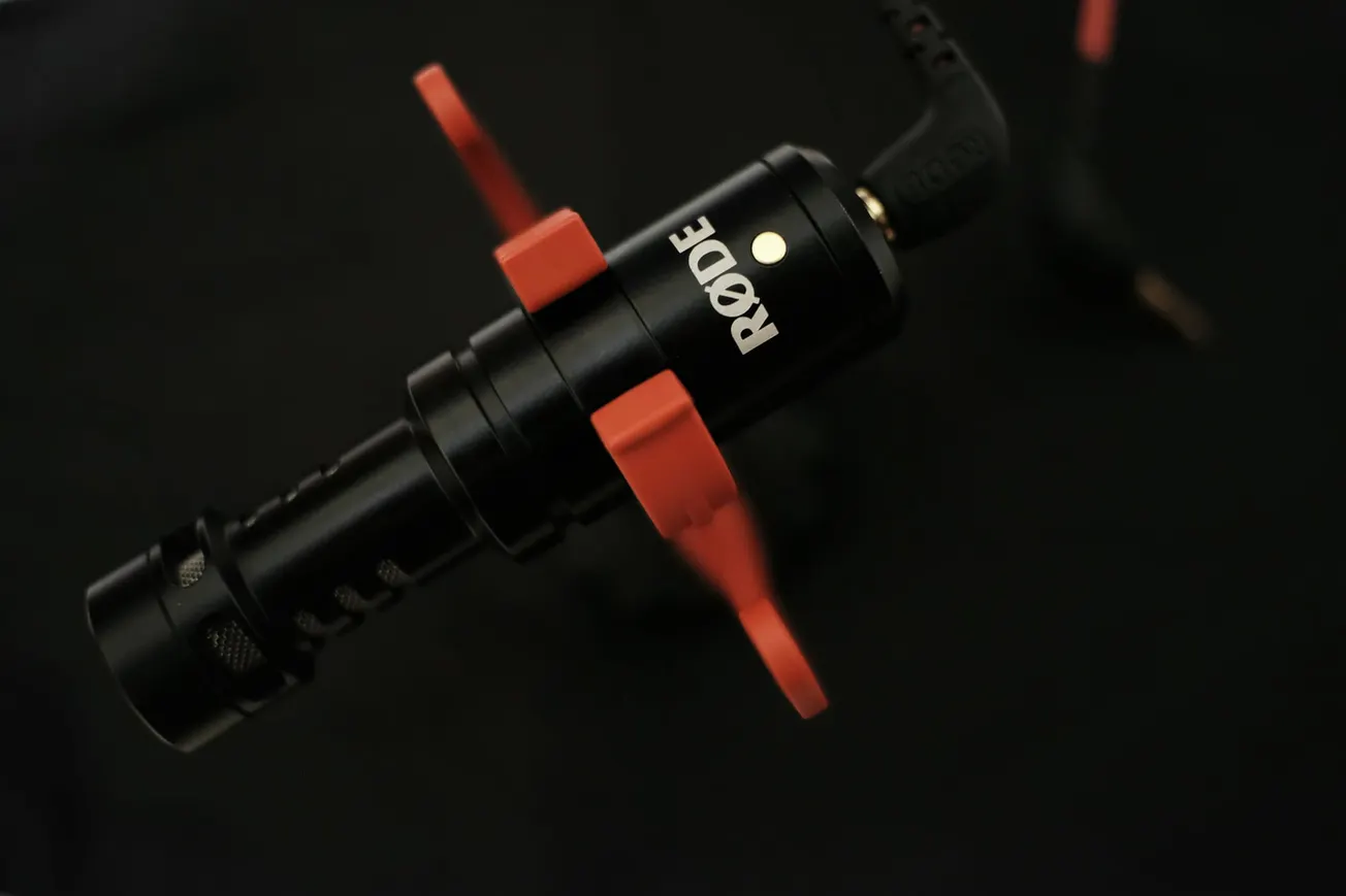 Close-up of a RØDE microphone with bright red shock mount against a dark background, highlighting its sleek black design and modern technology.