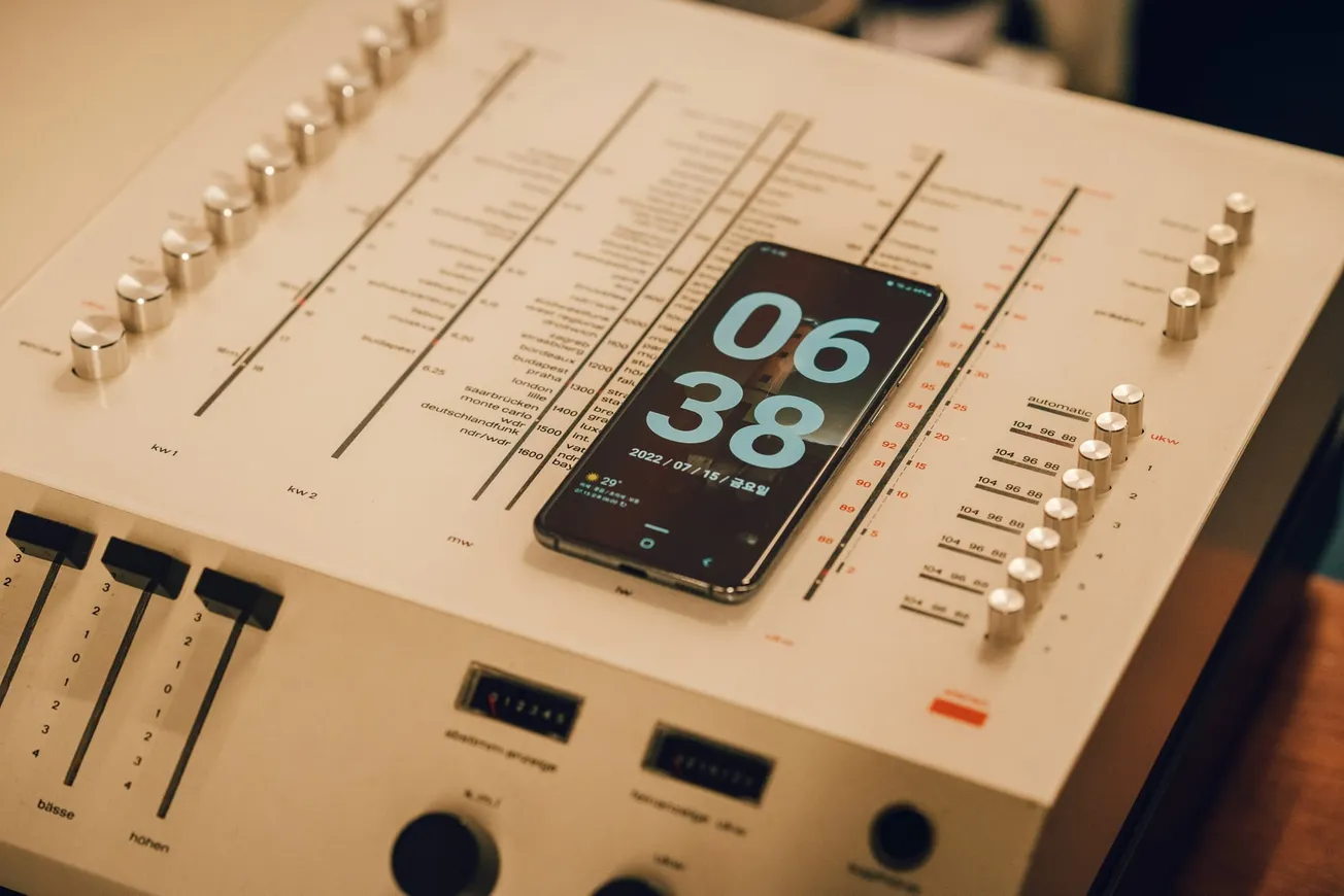 A smartphone displaying the time 06:38 rests on a vintage audio mixer. The mixer features sliders and dials, creating a retro, tech-focused ambiance.