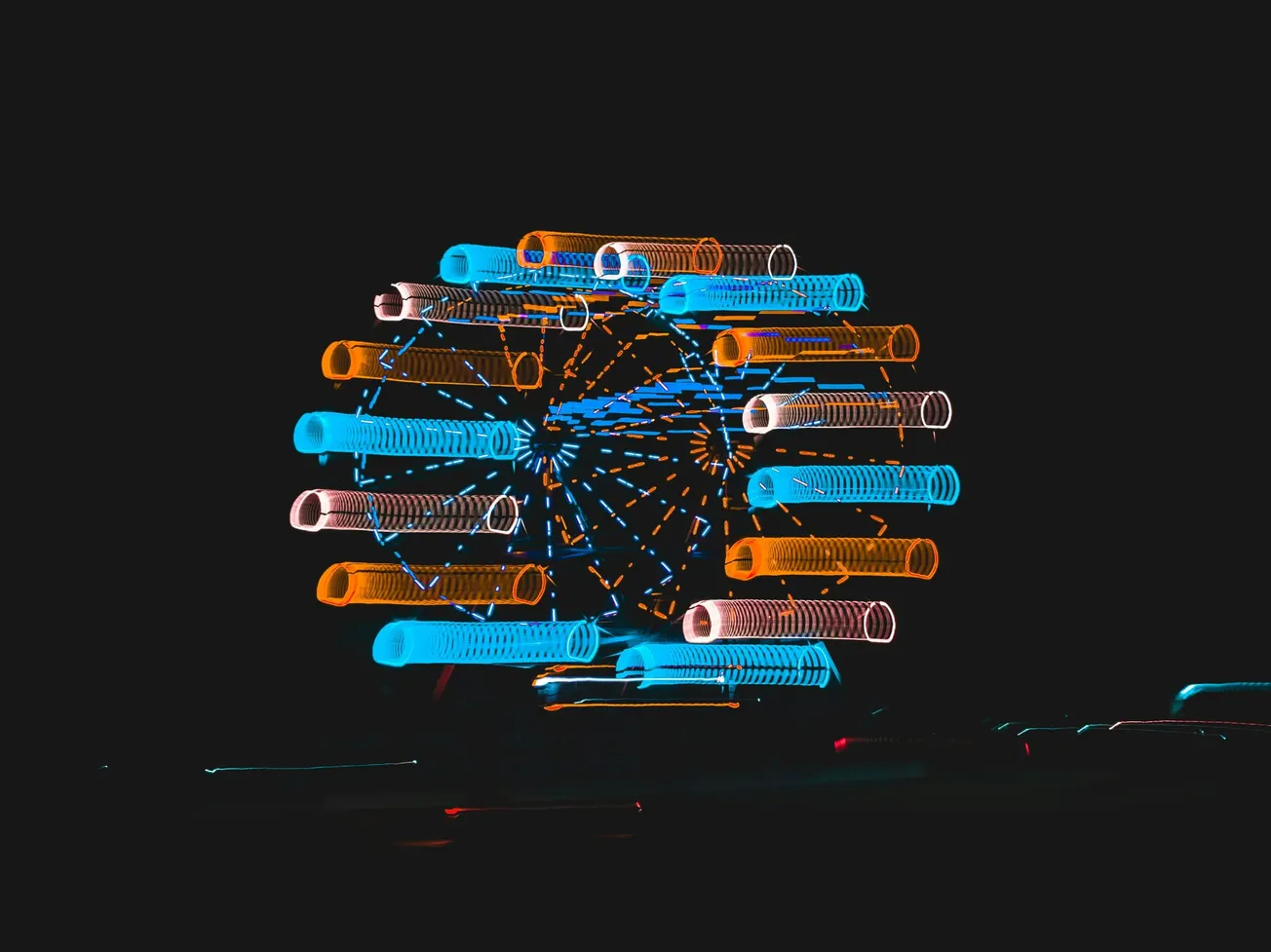 A vibrant Ferris wheel at night with motion blur, displaying radiant blue and orange lights against a dark background, creating a lively, dynamic scene.