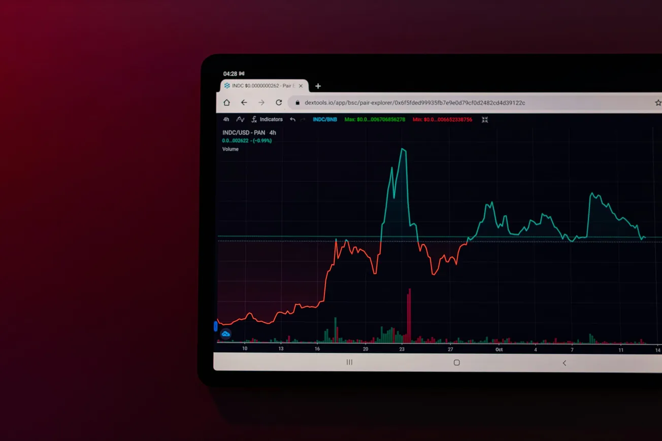 Cryptocurrency trading chart with a red and teal line graph on a dark background. The red line shows a sharp rise and fall, while the teal line remains steady with minor fluctuations.