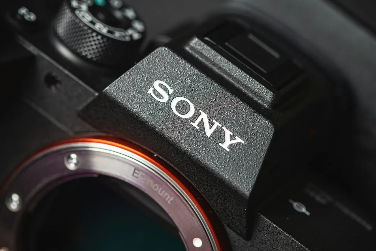 Close-up of a Sony camera body showing the mount with a metallic ring and the brand logo prominently displayed. The texture gives a modern, high-quality feel.