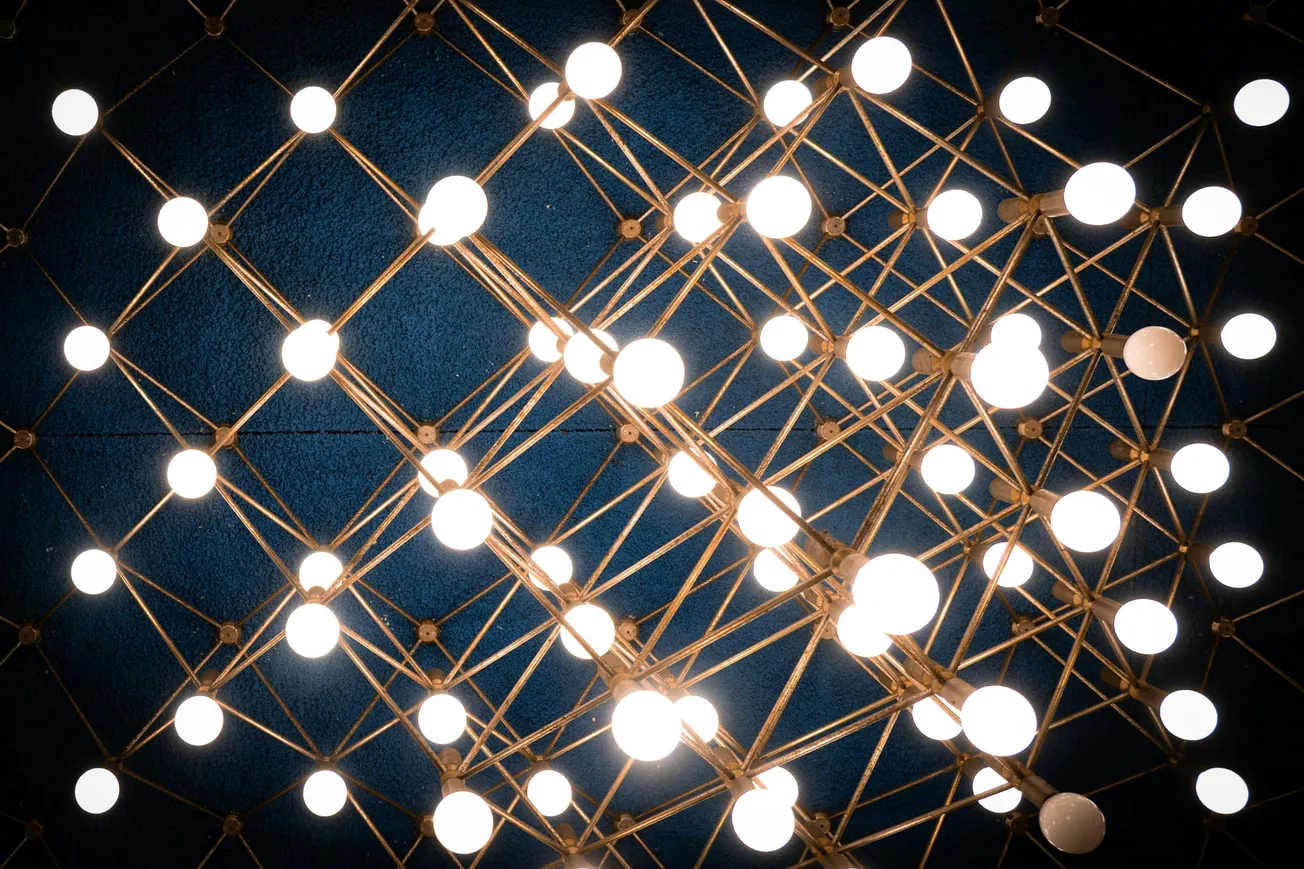 Ceiling light fixture with glowing round bulbs connected by intricate golden rods, forming a dynamic geometric pattern against a dark background.