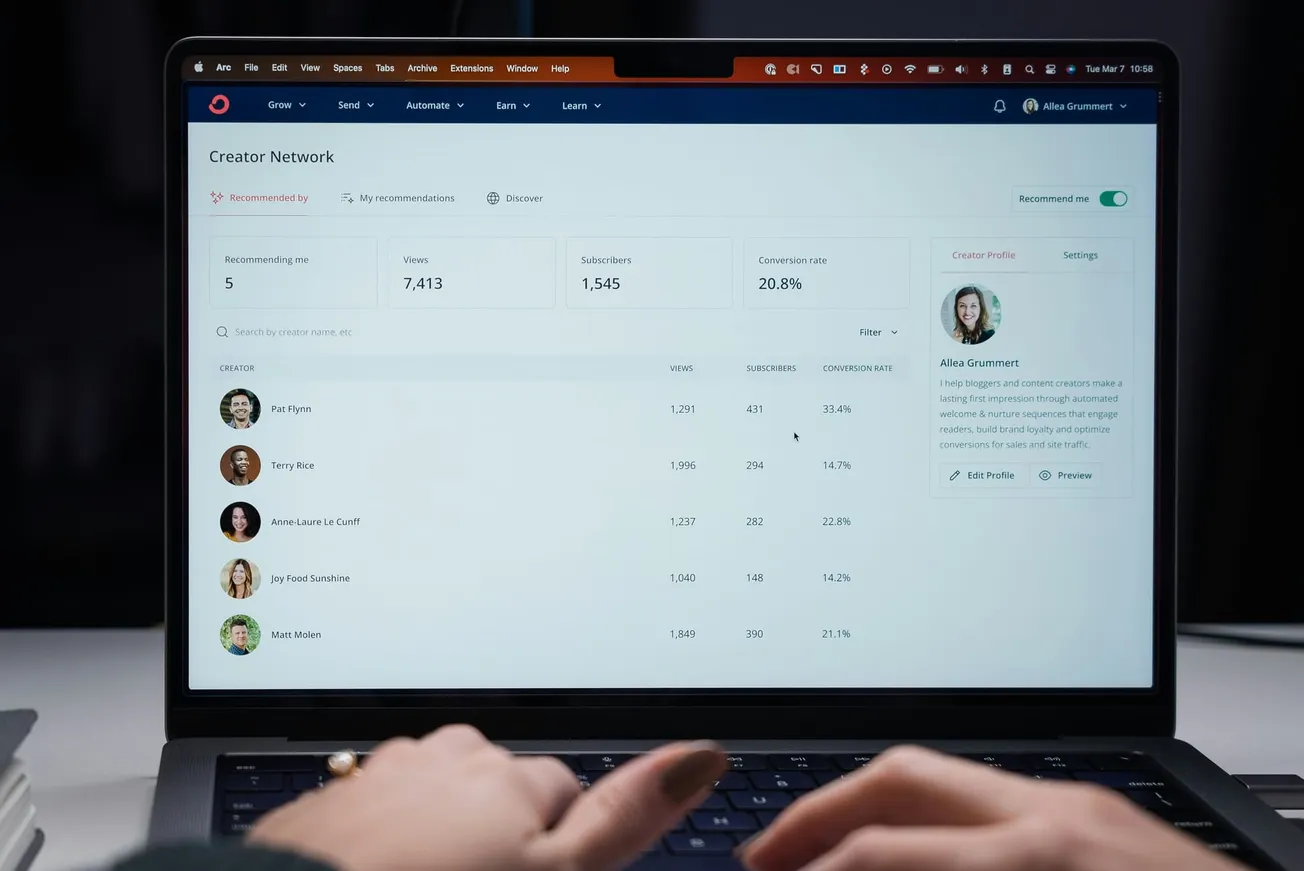 Laptop screen showing a "Creator Network" dashboard. Displays views, subscribers, and engagement rate. User's hand is on the keyboard, indicating interaction.