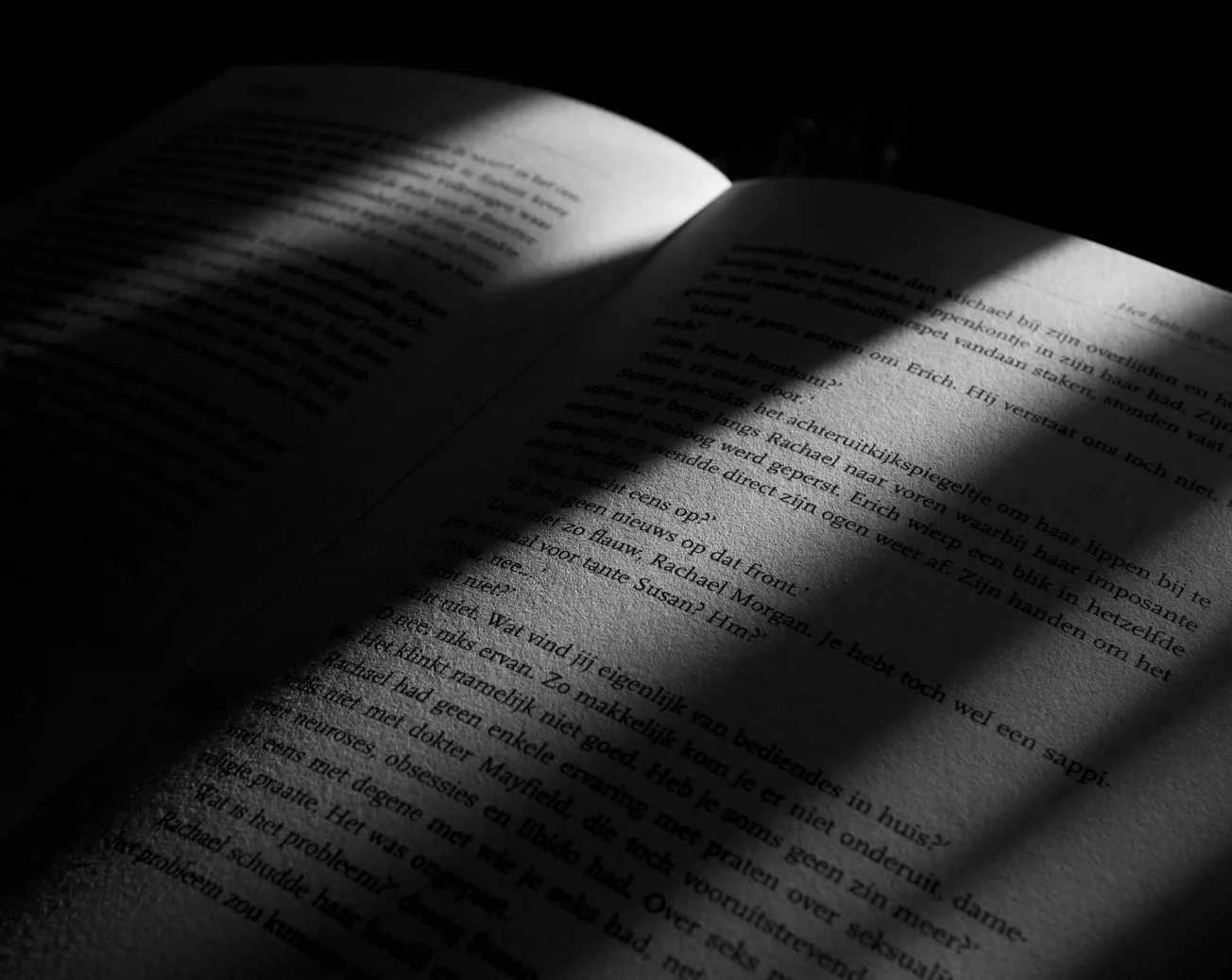 A dimly lit open book, with text in shadow and light streaming across the pages, creating a dramatic and mysterious atmosphere.