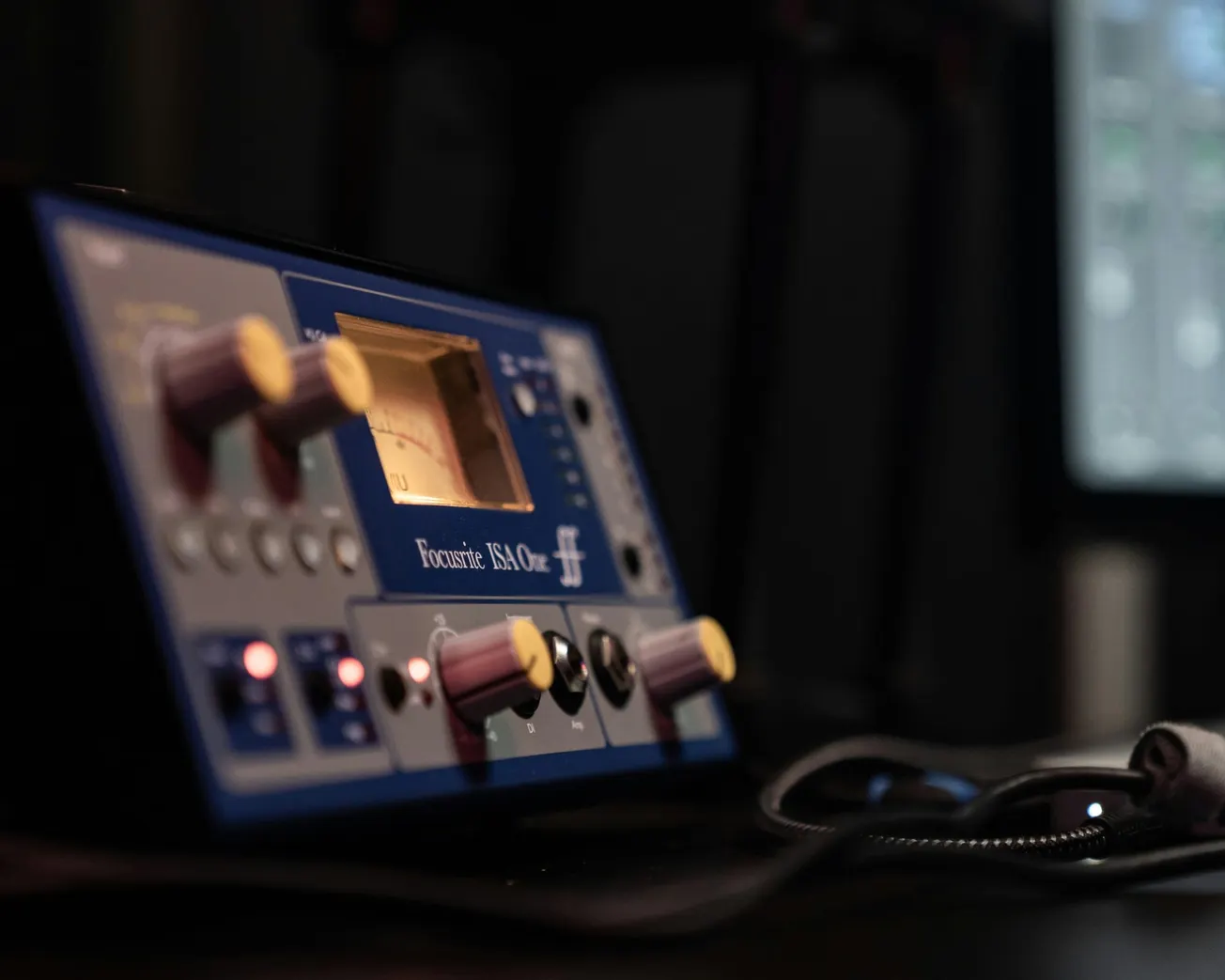 A Focusrite audio interface with yellow knobs, buttons, and a glowing display is set in a dimly lit studio, conveying a professional music production atmosphere.