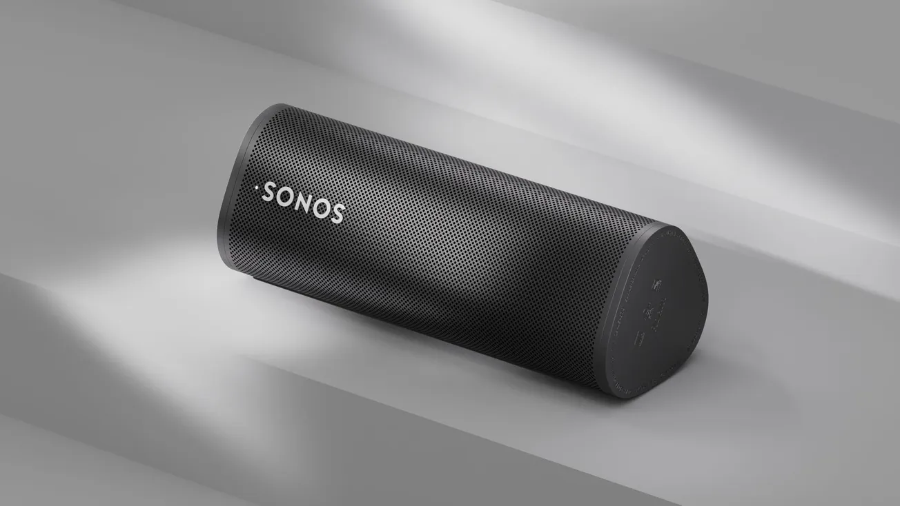 A sleek black Sonos portable speaker rests on a light gray surface. Sunlight casts soft shadows, emphasizing its modern design and minimalist aesthetic.