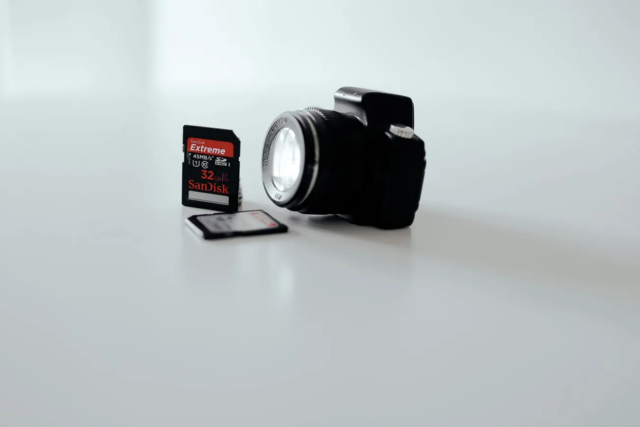 A DSLR camera is focused in the background on a white surface, with two SanDisk memory cards placed in the foreground, creating a minimalist and professional tone.